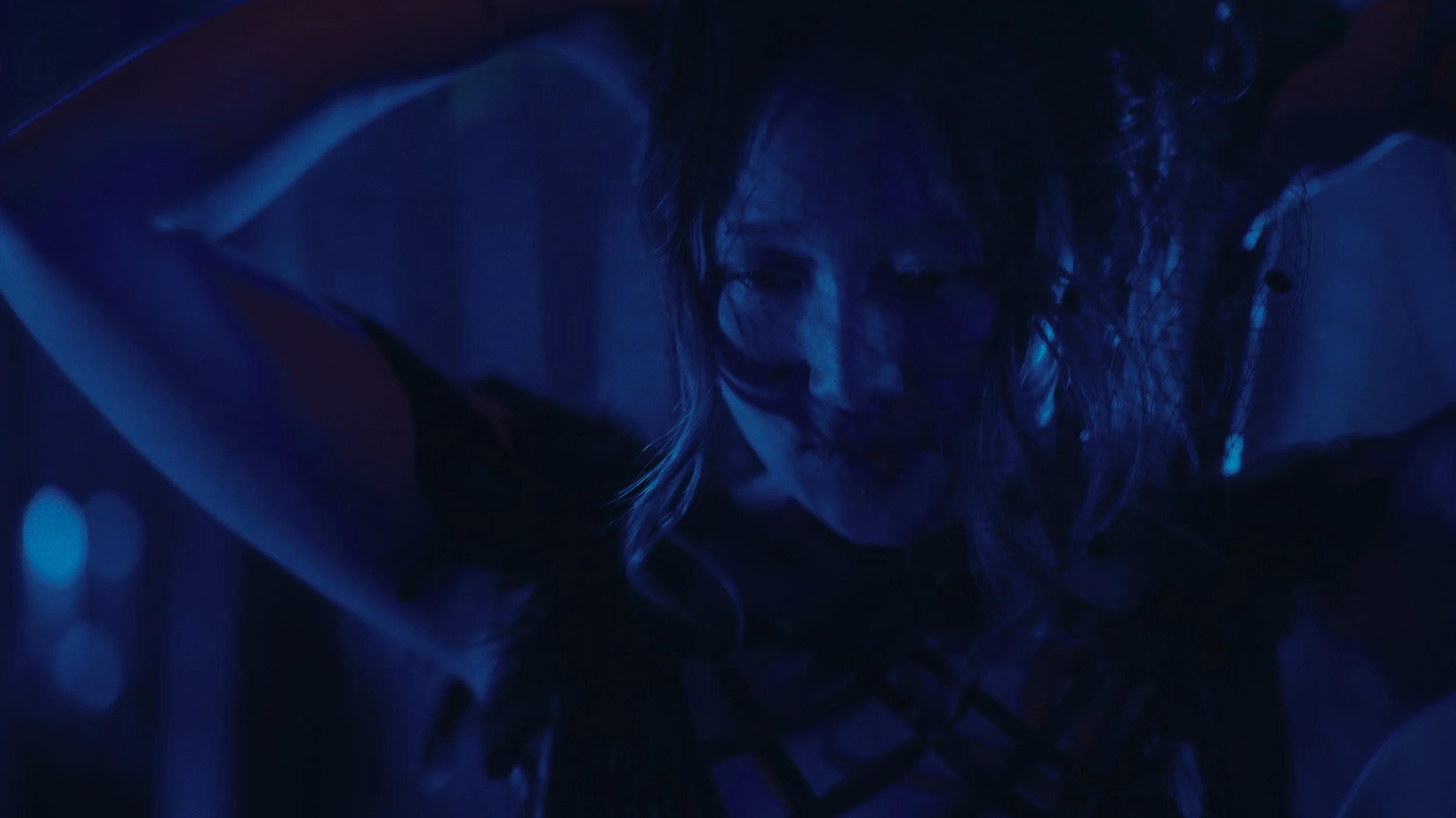 Una donna con capelli scombinati in un'illuminazione blu scura, in una posa intensa e drammatica.