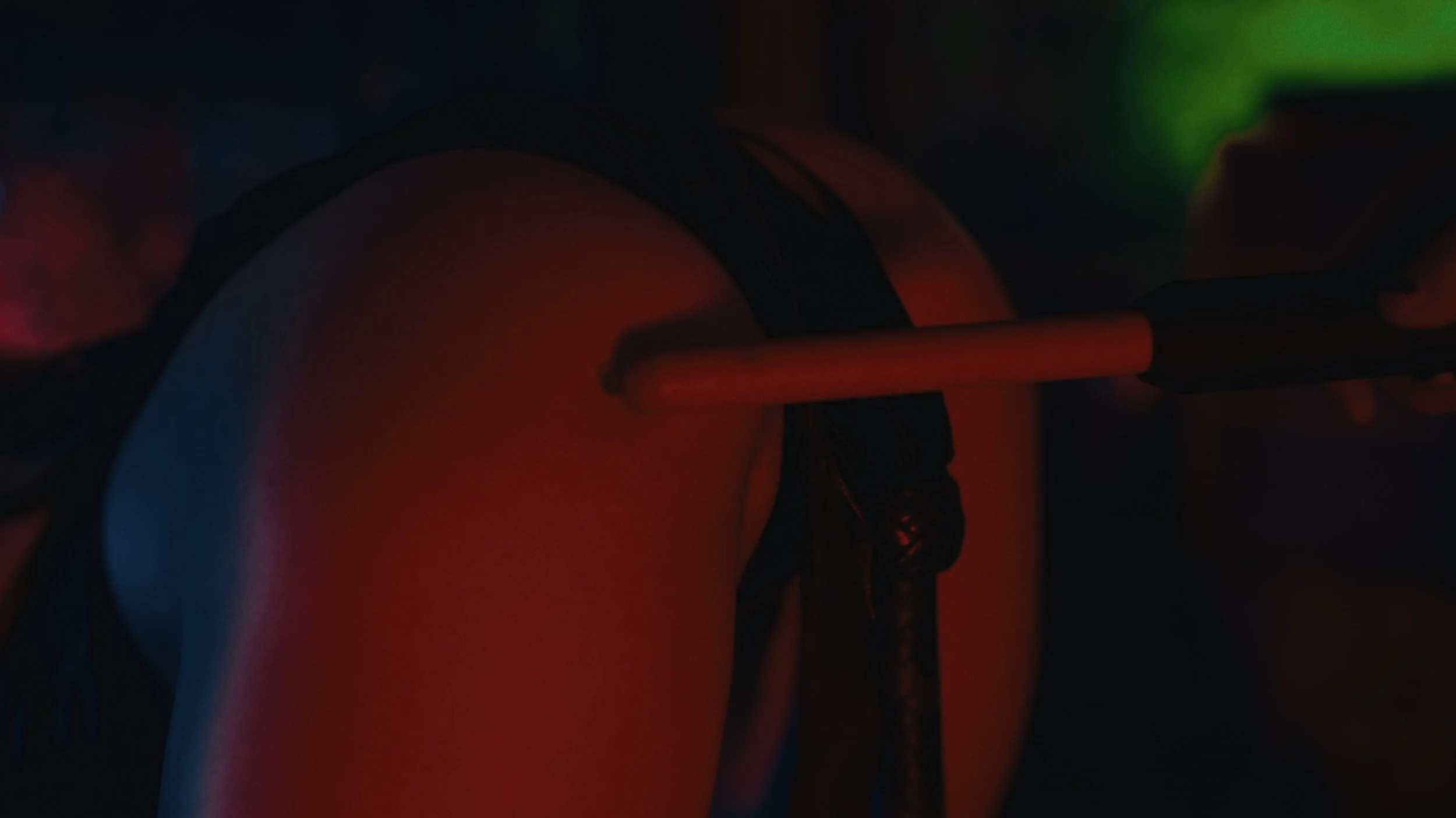 Close-up di una persona con shorts neri che si toglie un oggetto, con sfondo scuro illuminato da luci colorate.