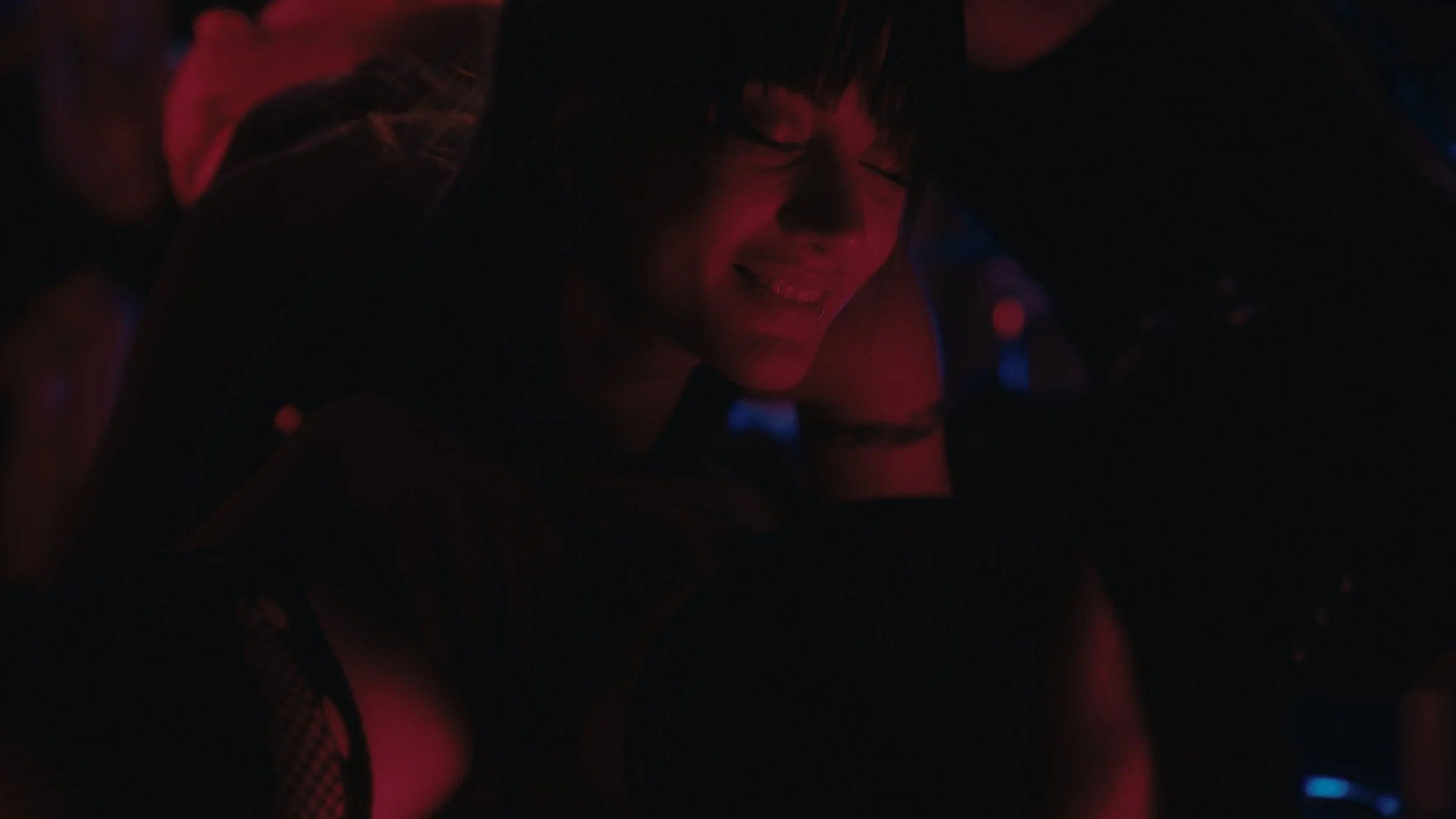 Una donna sorridente mentre si ispira in un ambiente oscuro con luci colorate.