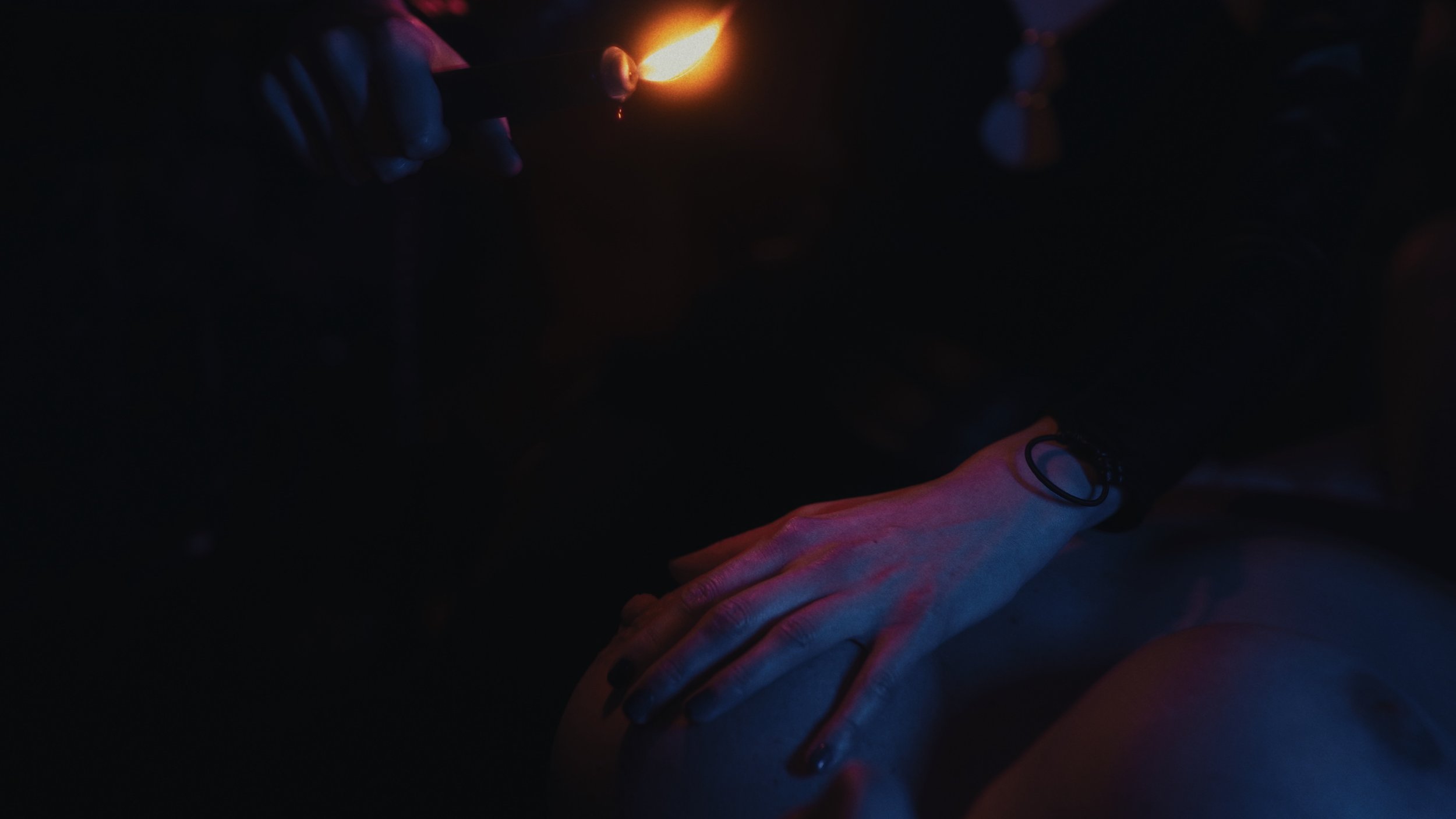 Una persona accende un fiammifero a notte, illuminando leggermente il volto e le mani, in un ambiente oscuro.