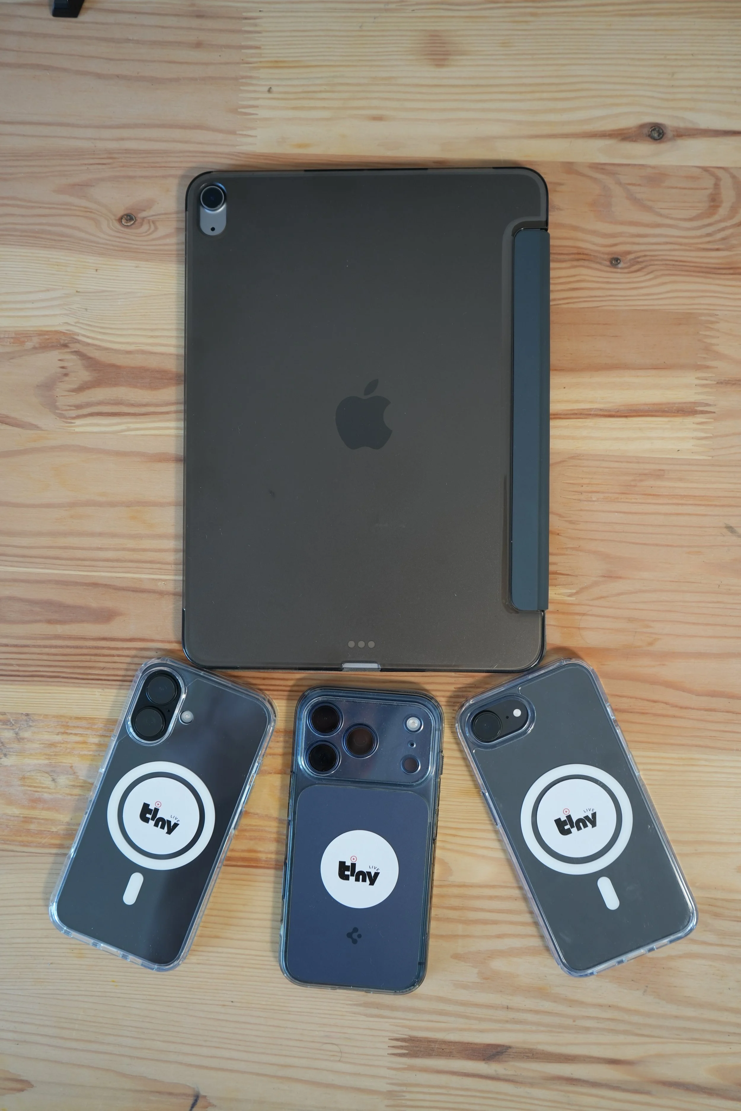 Une tablette Apple posée sur une table en bois, entourée de plusieurs téléphones iPhone dans des étuis de protection avec le logo "thv".