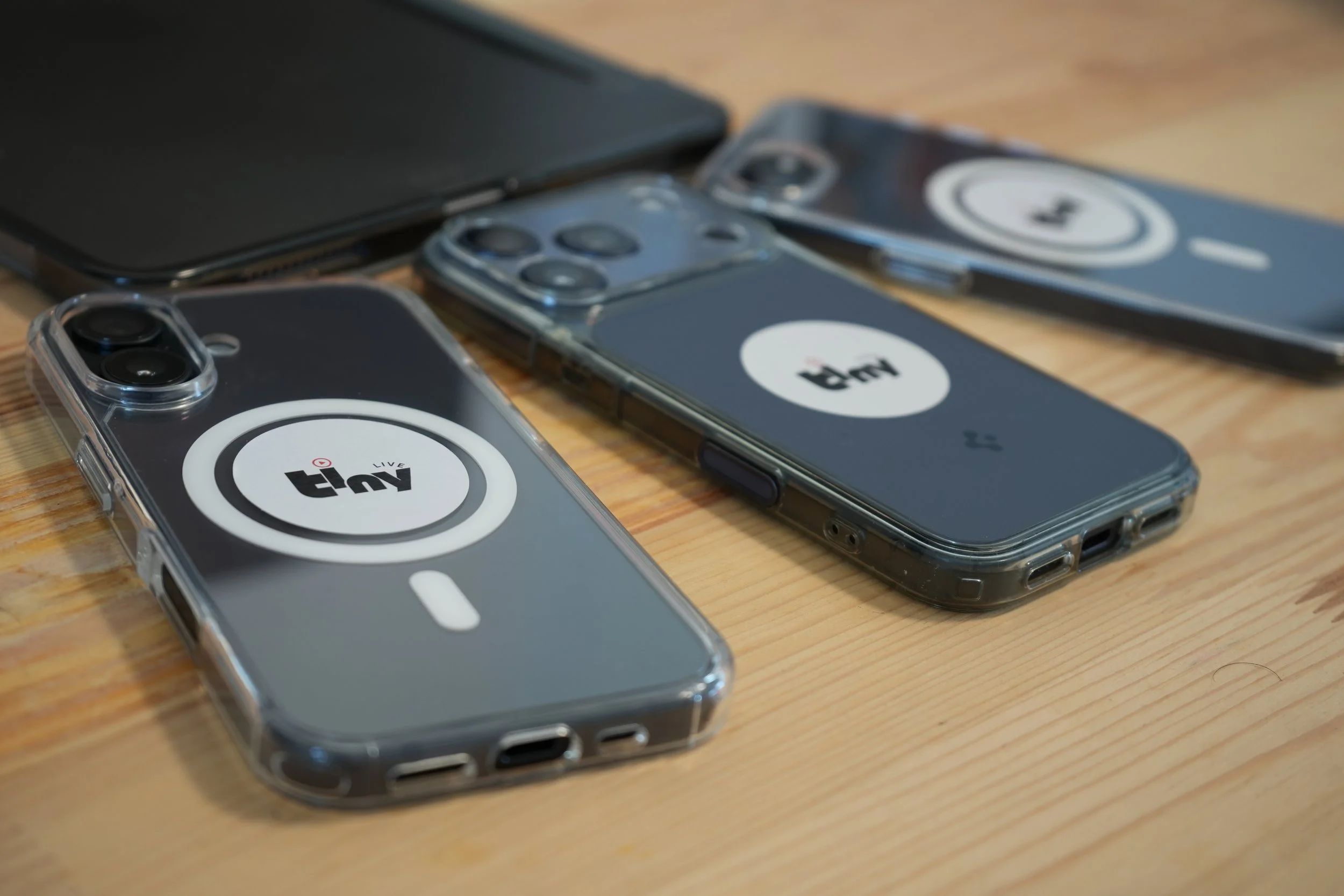 Plusieurs téléphones portables avec des coques transparentes portant le logo de tnt live, placés sur une surface en bois.