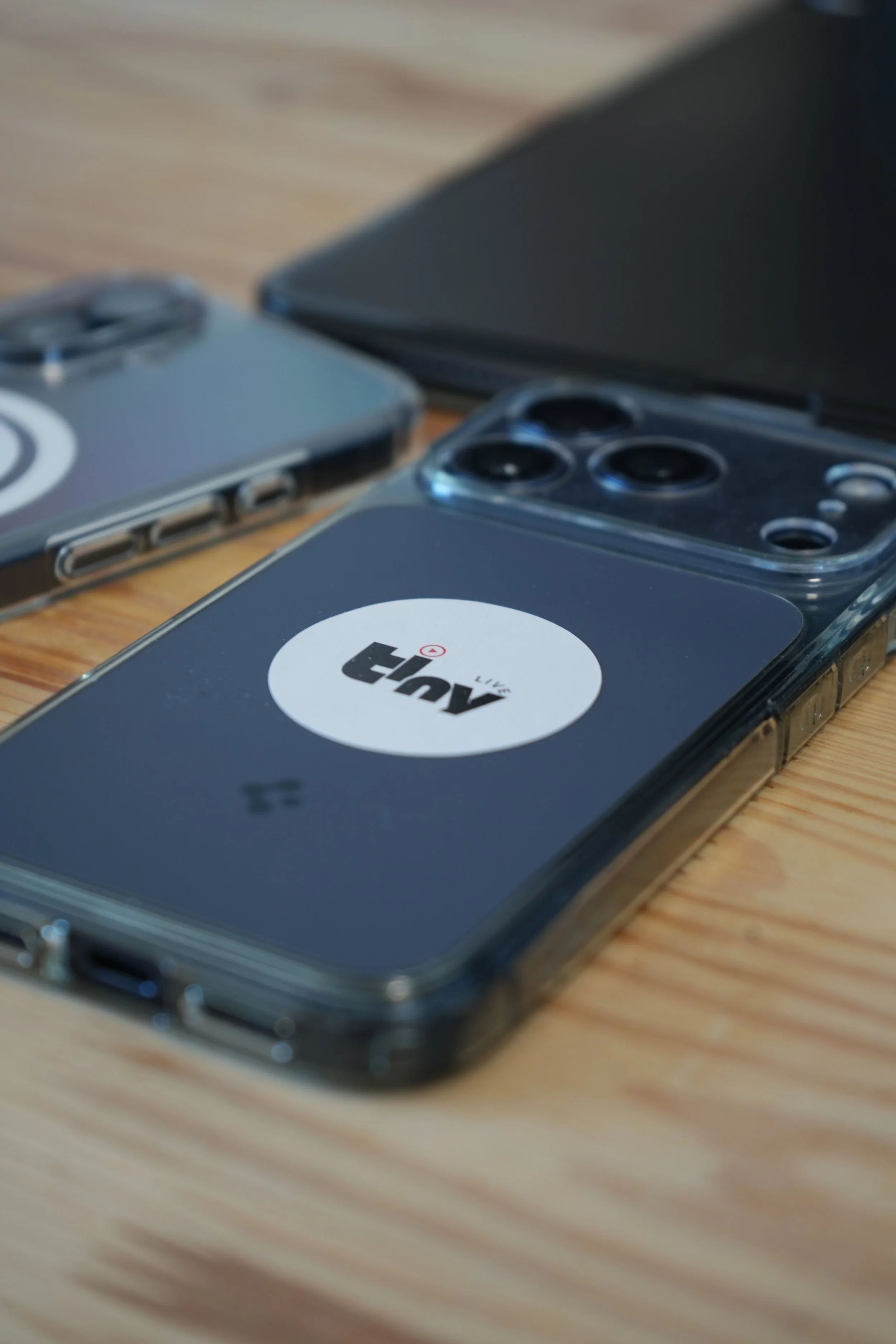Deux téléphones portables modernes sont posés sur une surface en bois, avec des étuis transparents où il est écrit "TinyLive"