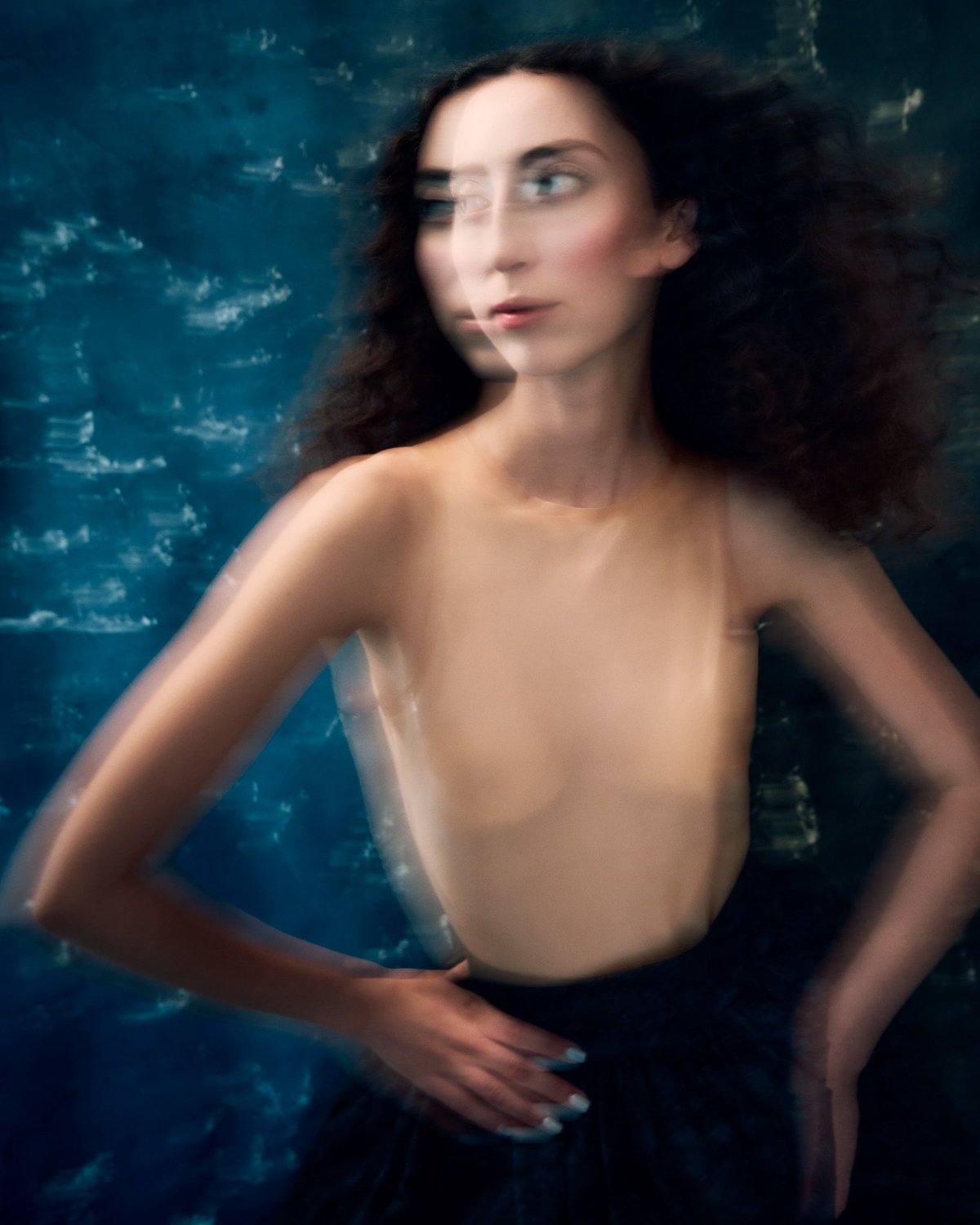 A woman with dark curly hair is partially submerged in water, with a blurred effect that makes her face appear to move.