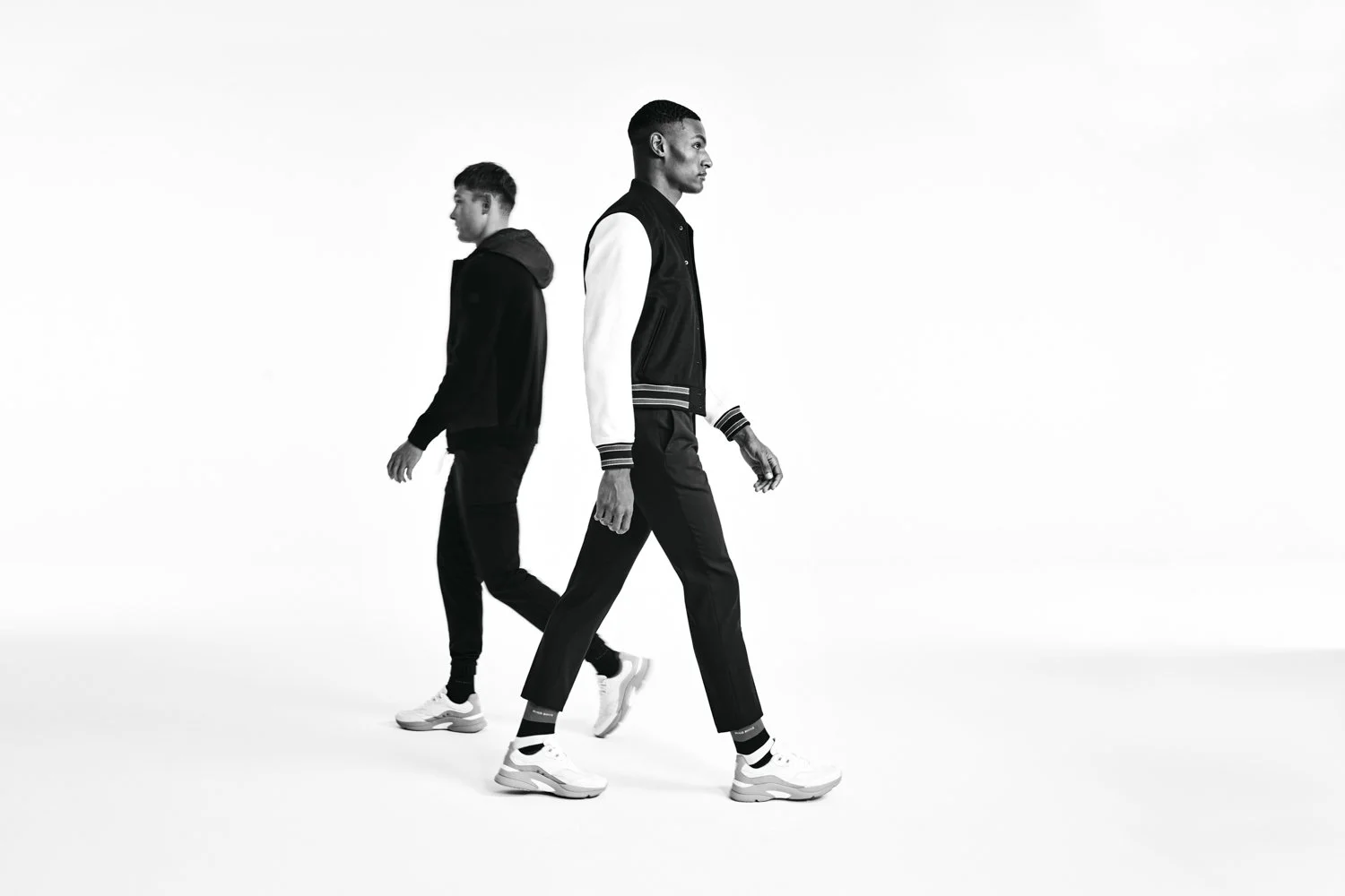 Two young men walking in opposite directions in a minimalist black and white photo, wearing casual sportswear and sneakers.