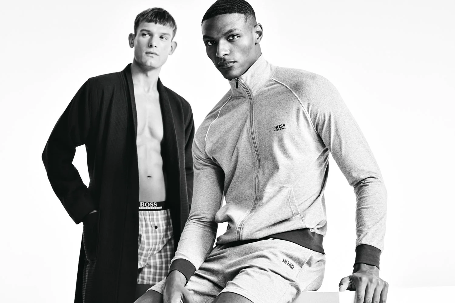 Two male models wearing BOSS athletic wear against a plain white background, black and white photo.