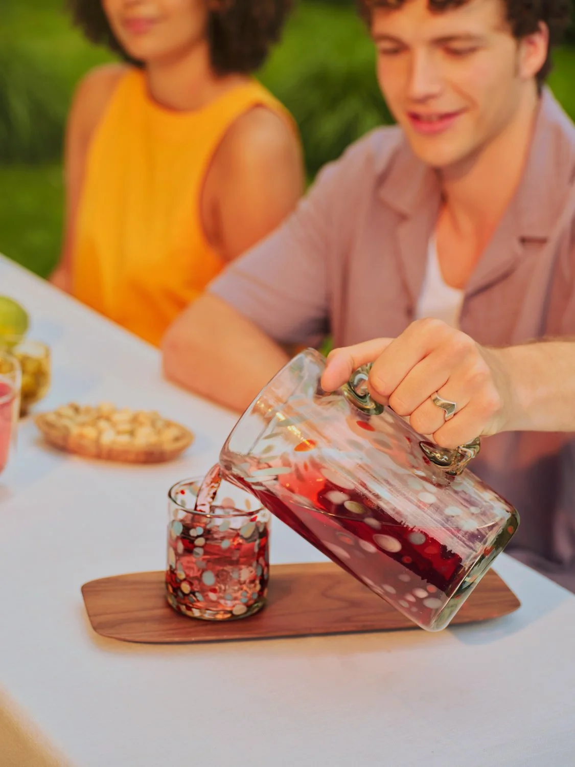 Person pouring red drink into a glass on a table at an outdoor gathering.