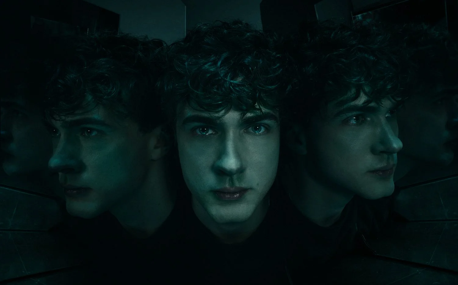 A person looking into a reflective black surface with three reflections, with a dark background.