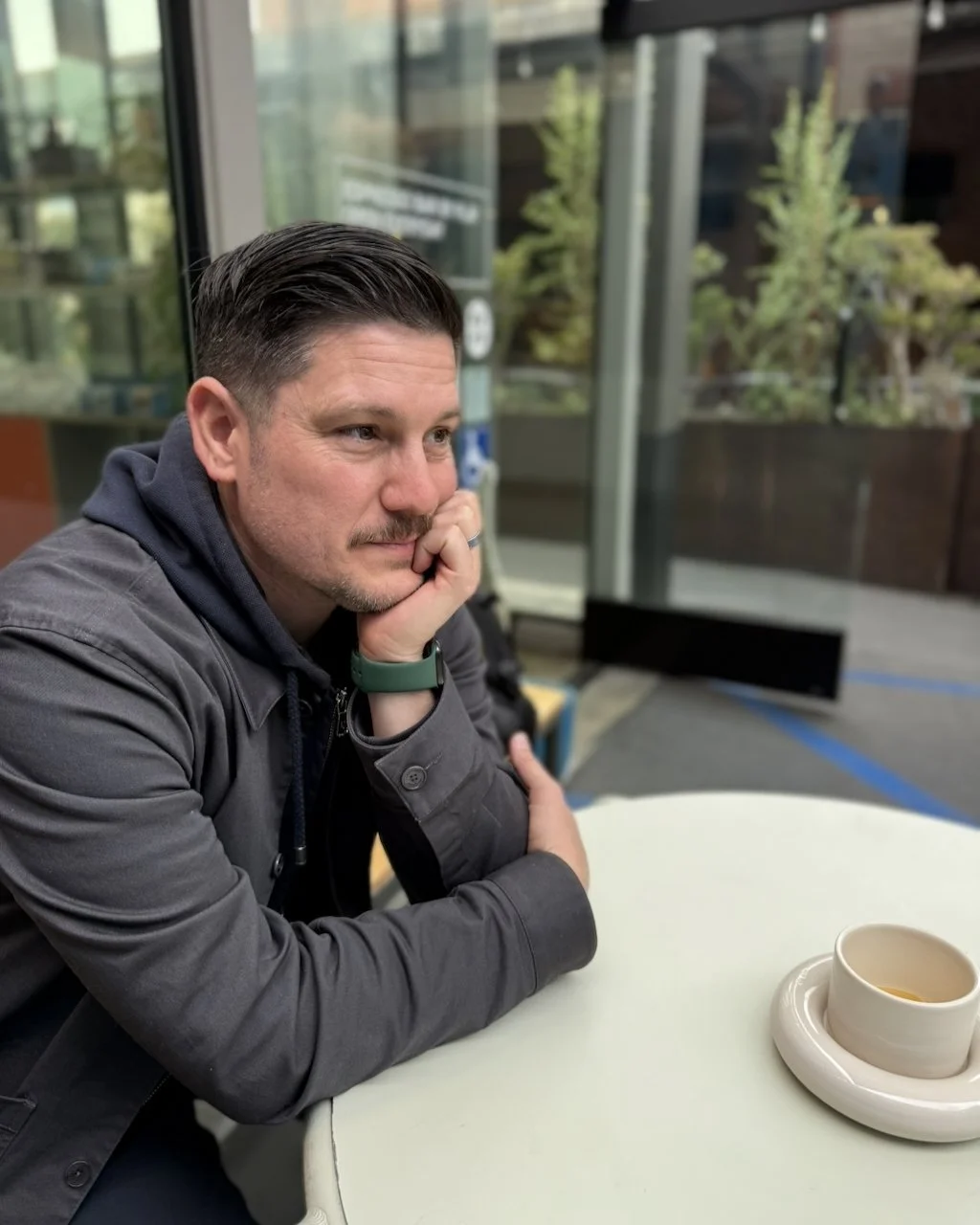 Man sitting at a cafe table with his chin resting on his hand beside a cup of coffee