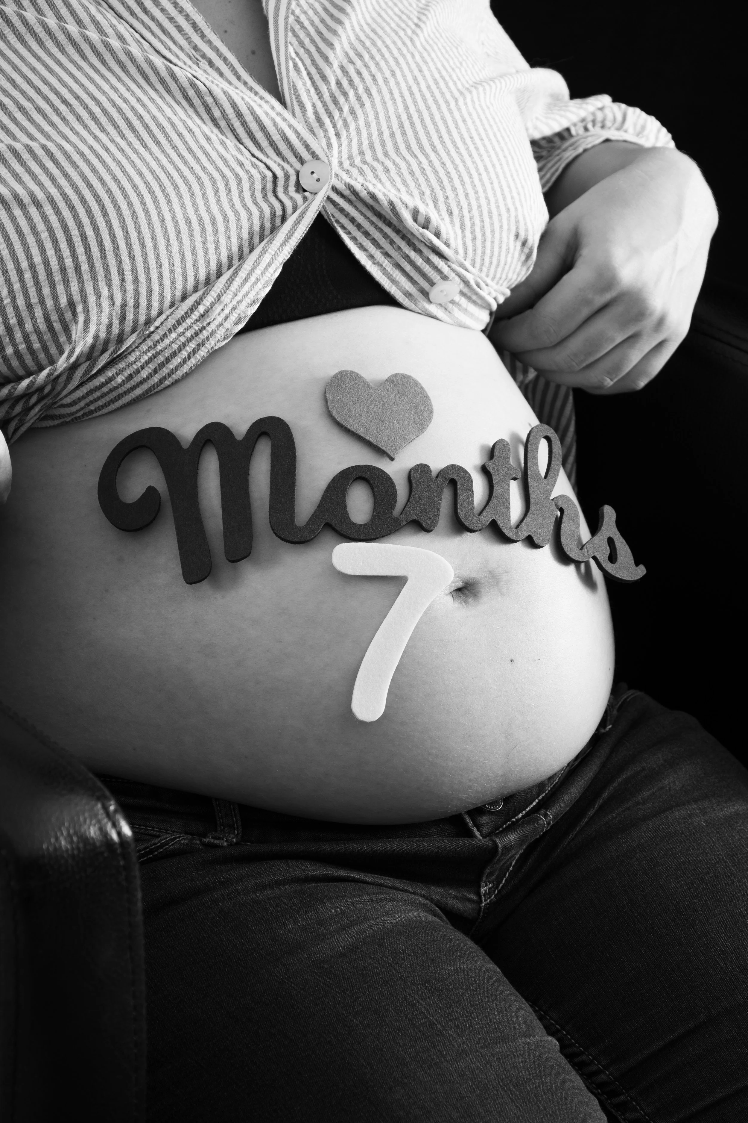 Ventre arrondi d'une femme enceinte avec un panneau indiquant 'Maman 7' et un cœur en décoration, en noir et blanc.