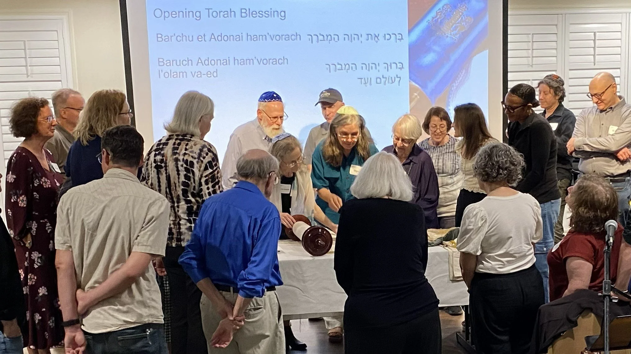Members gather with Cantor Gostein for a Torah dedication service in Austin, March 2026, with the blessing on screen.