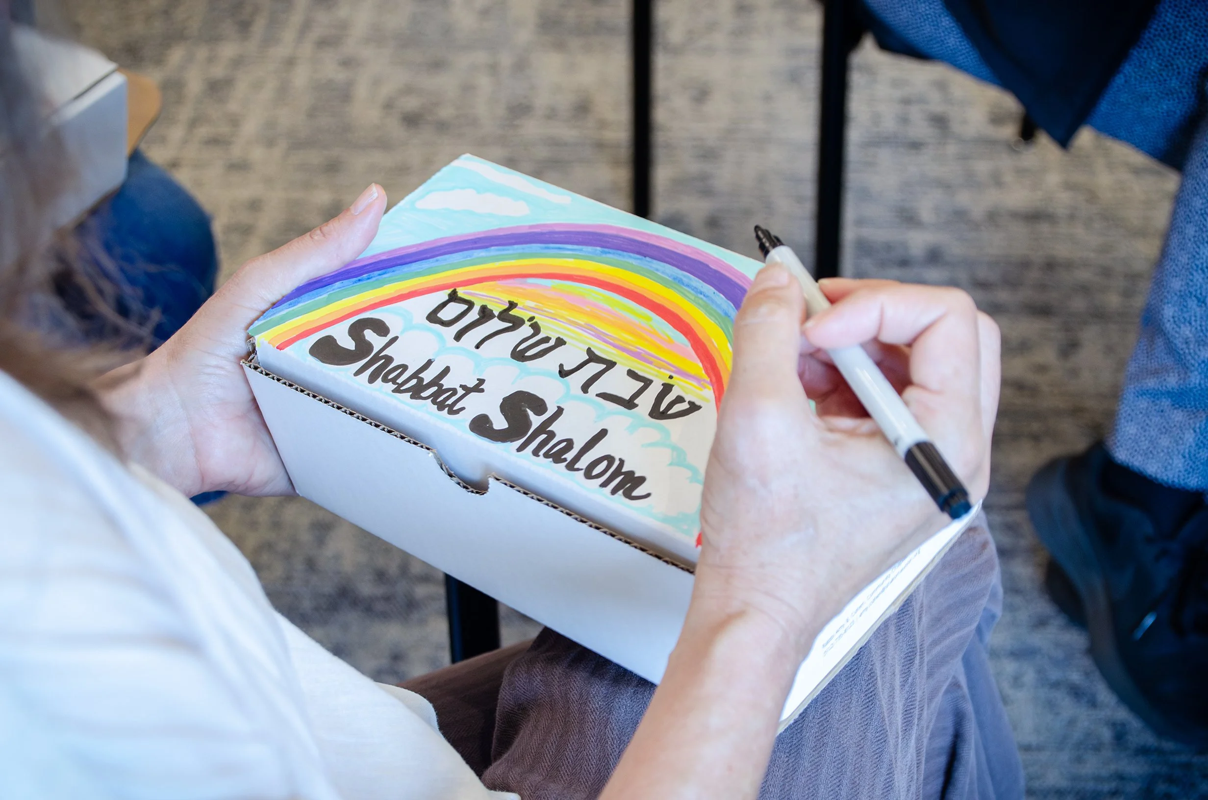 Kol Shira member coloring a Shabbat Shalom rainbow on her Shabbat Box.