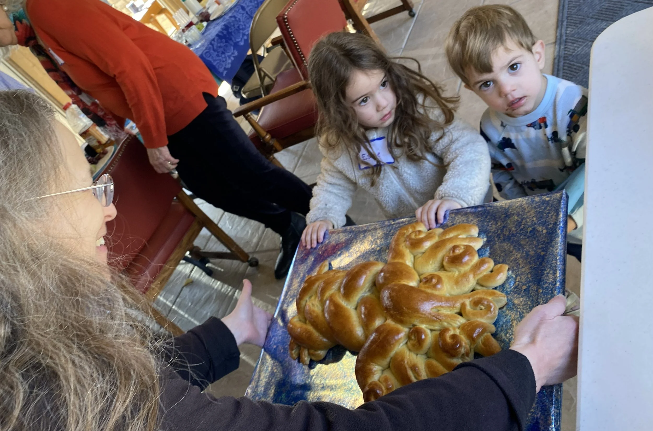 Cantor Gostein offering a tree-shaped challah to two quizzical toddlers at a Kol Shira family gathering in Austin.