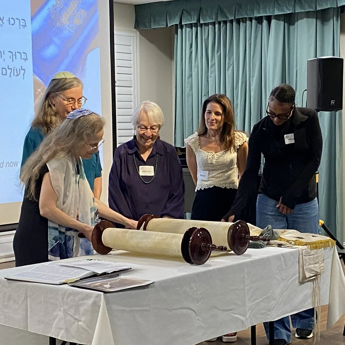 Several Kol Shira members gather around the Sefer Torah as Cantor Abby Gostein assists them in preparing to read during the dedication service in Austin.