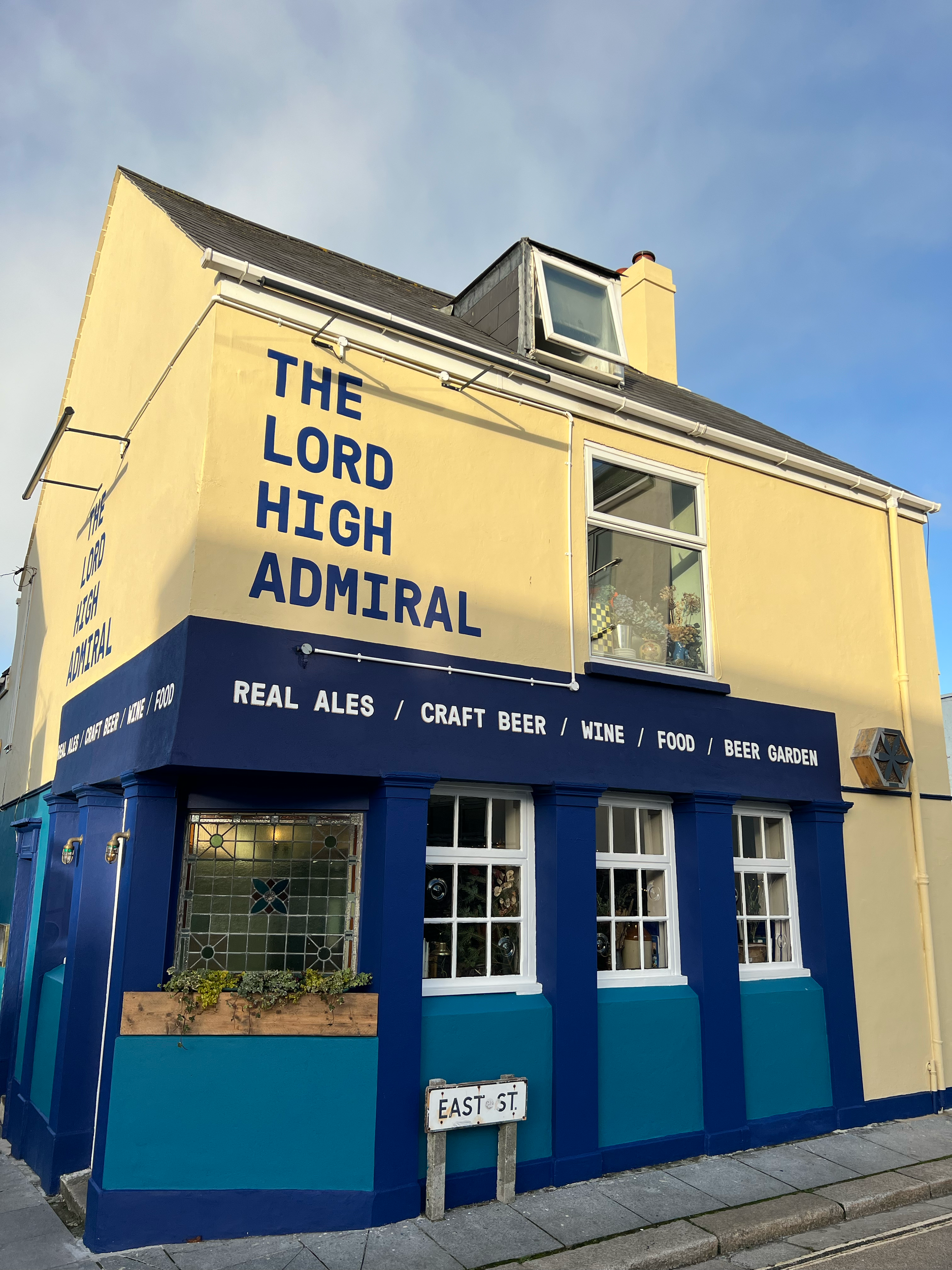 The Laurel Admiral building exterior with yellow walls and blue accents, featuring a sign indicating it sells real ale, craft beer, food, and has a beer garden.