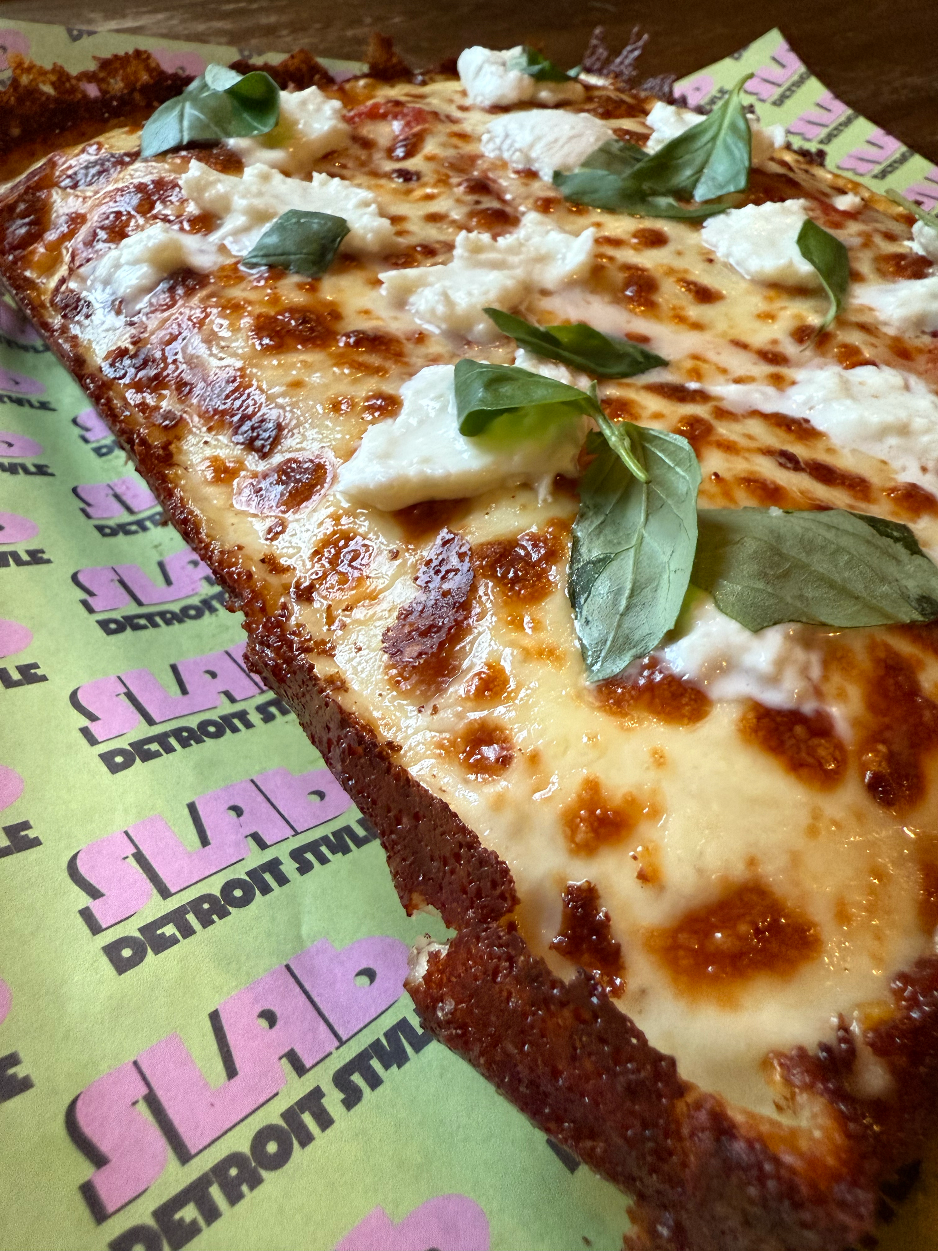 A slice of Italian pizza with cheese, basil leaves, and a crispy crust.