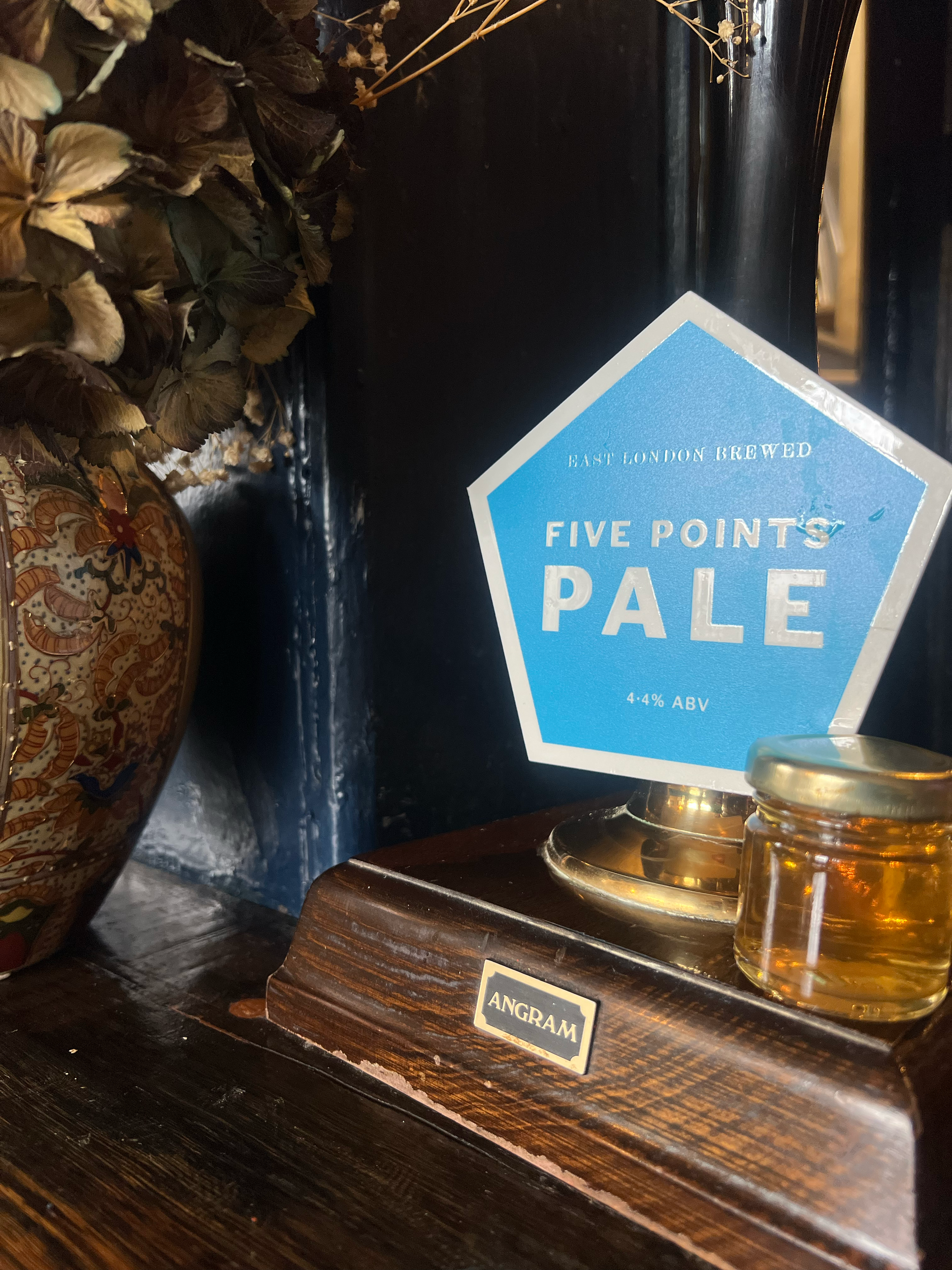 A glass of beer on a wooden table with a blue sticker that reads 'Five Point Pale, 4.4% ABV, Nashville, London Brewed'.