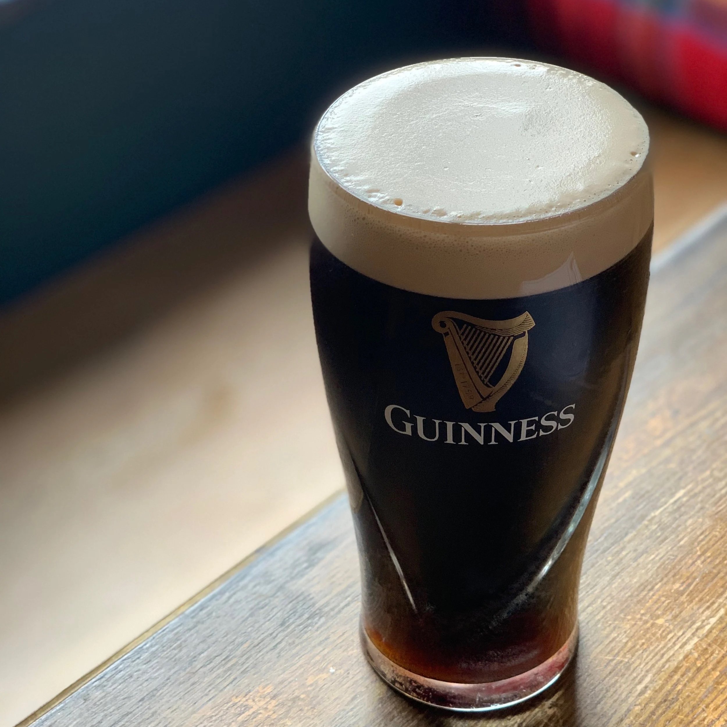 A pint glass of Guinness stout beer with a thick creamy head on top, sitting on a wooden surface.
