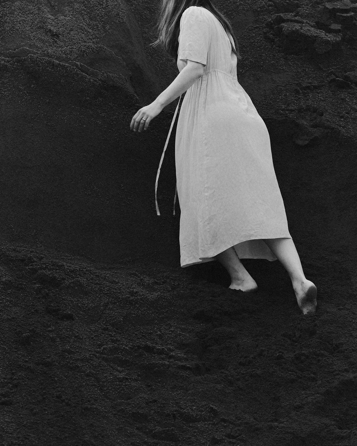 Una donna con un vestito lungo, senza scarpe, che cammina sulla sabbia nera.