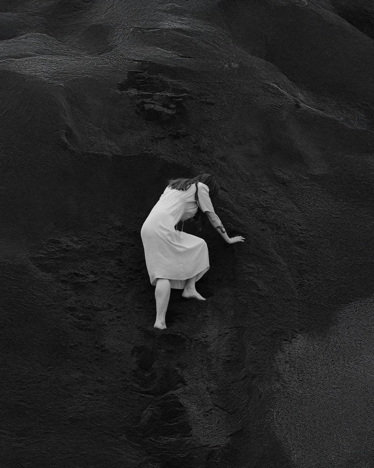 Una donna in vestito bianco che si arrampica su una superficie scura e rocciosa.