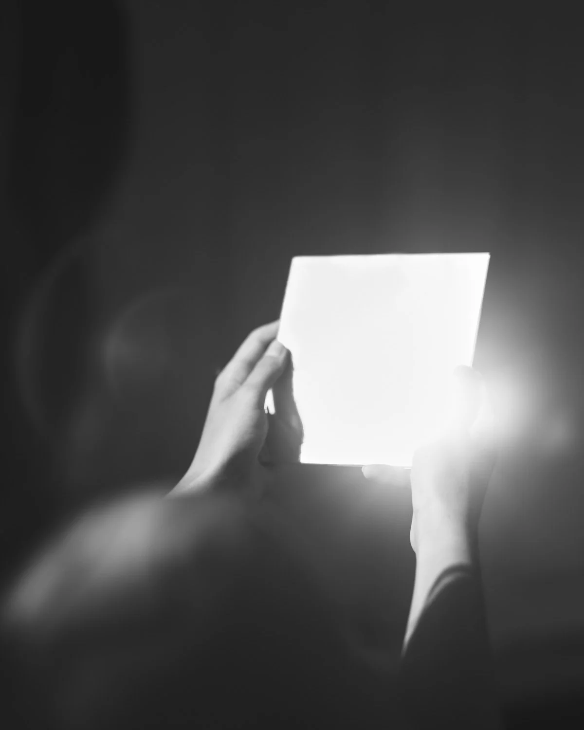 Persona che tiene una scatola luminosa in mano, visibile solo il contorno delle mani, in un ambiente oscuro.