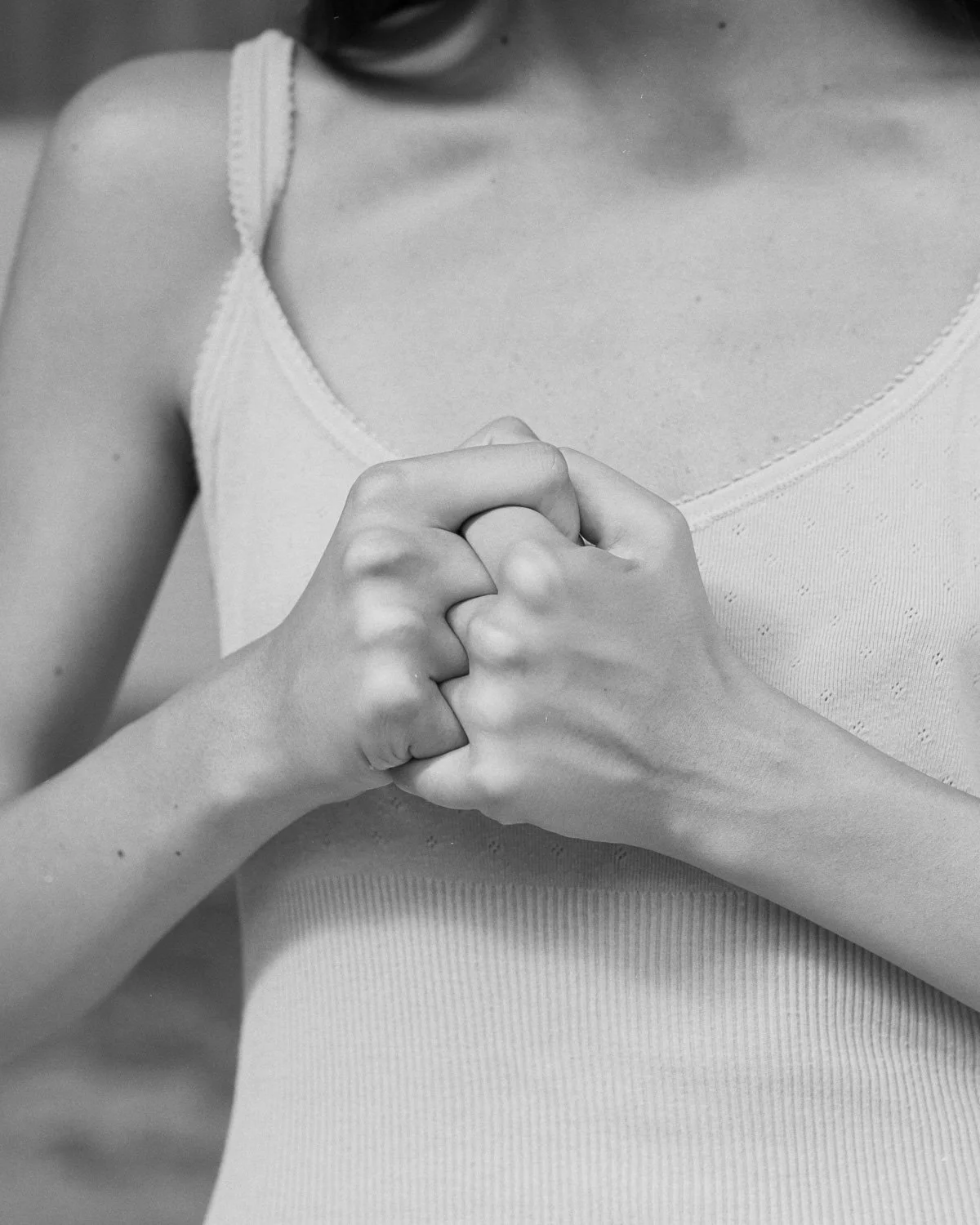 Mani incrociate in primo piano, torso di una donna in canottiera, in bianco e nero.