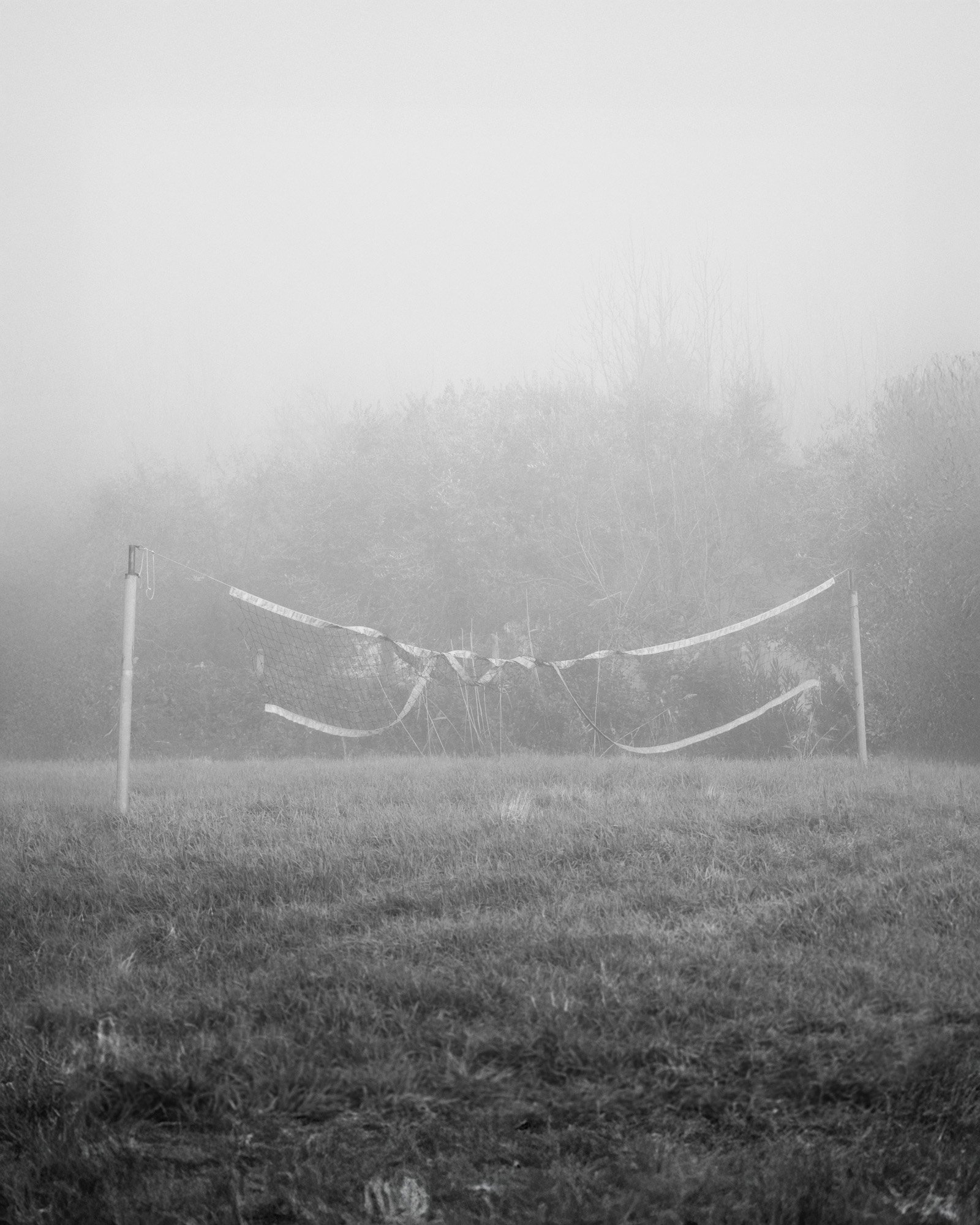 Un campo di erba con una rete da volley sportiva abbattuta e avvolta dalla nebbia.
