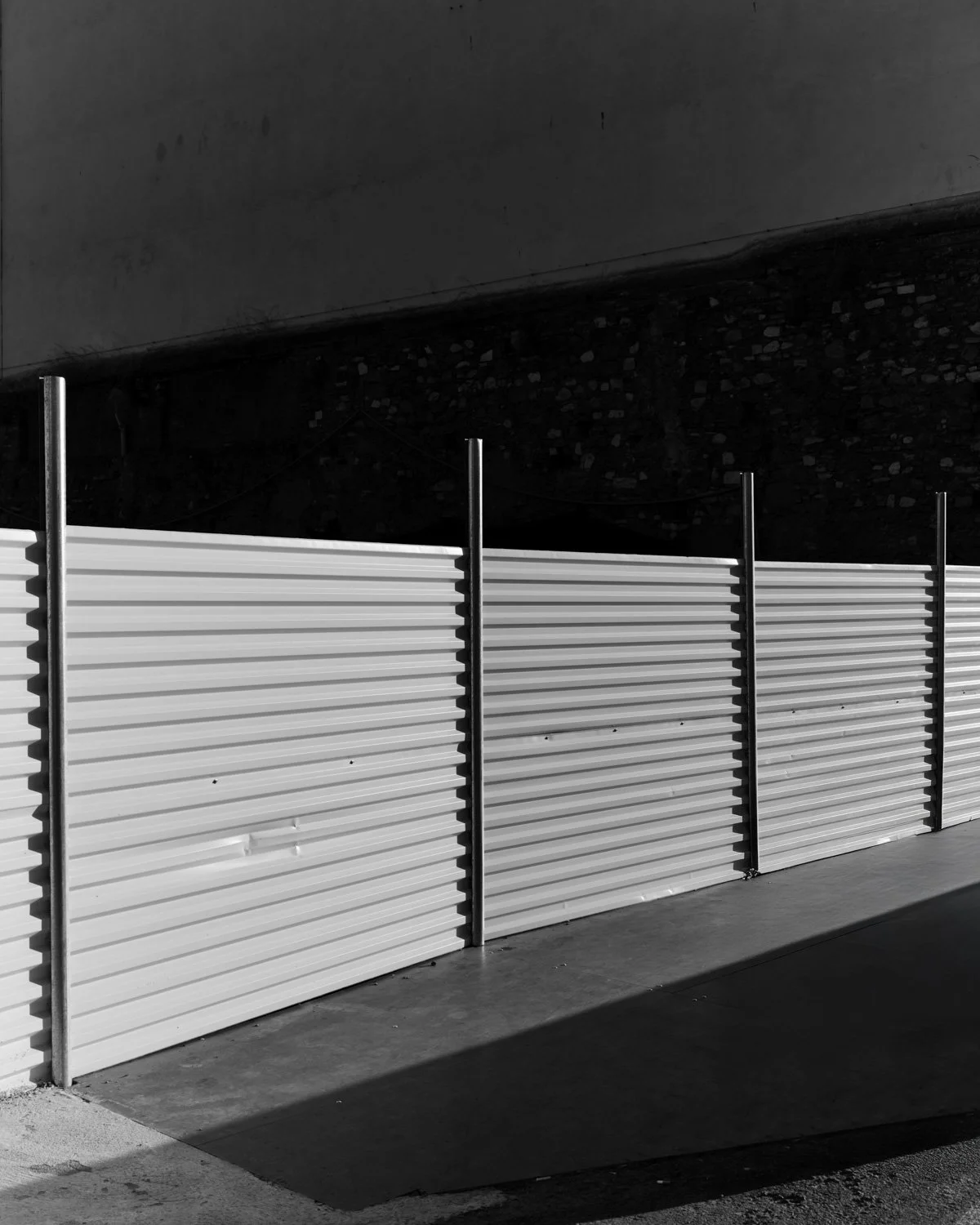 Recinzione bianca in metallo in primo piano con sfondo di muro scuro in una scena in bianco e nero.