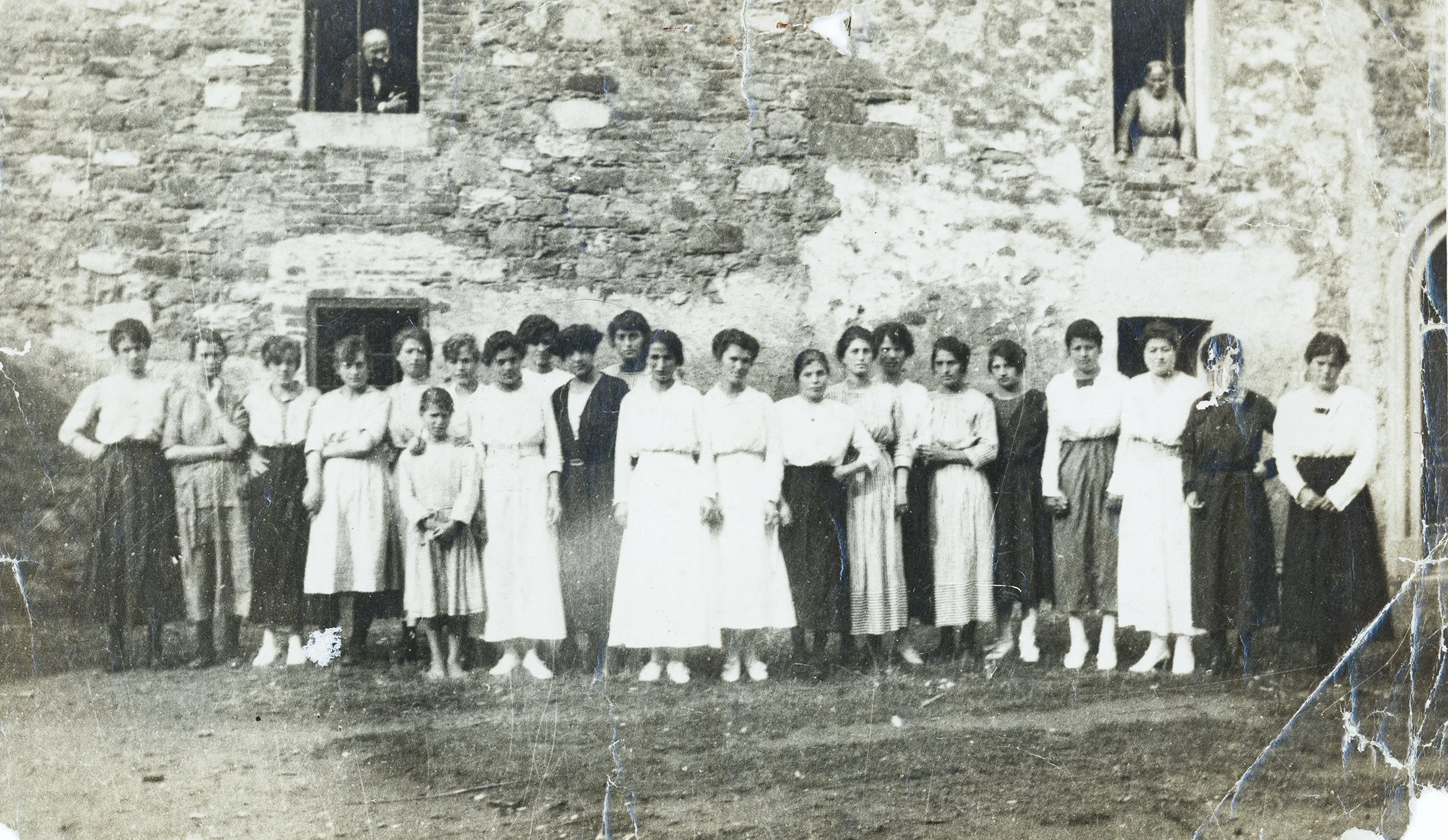 Gruppo di persone, donne e bambini, che posano davanti a un edificio in pietra, probabilmente in un contesto storico, in bianco e nero.