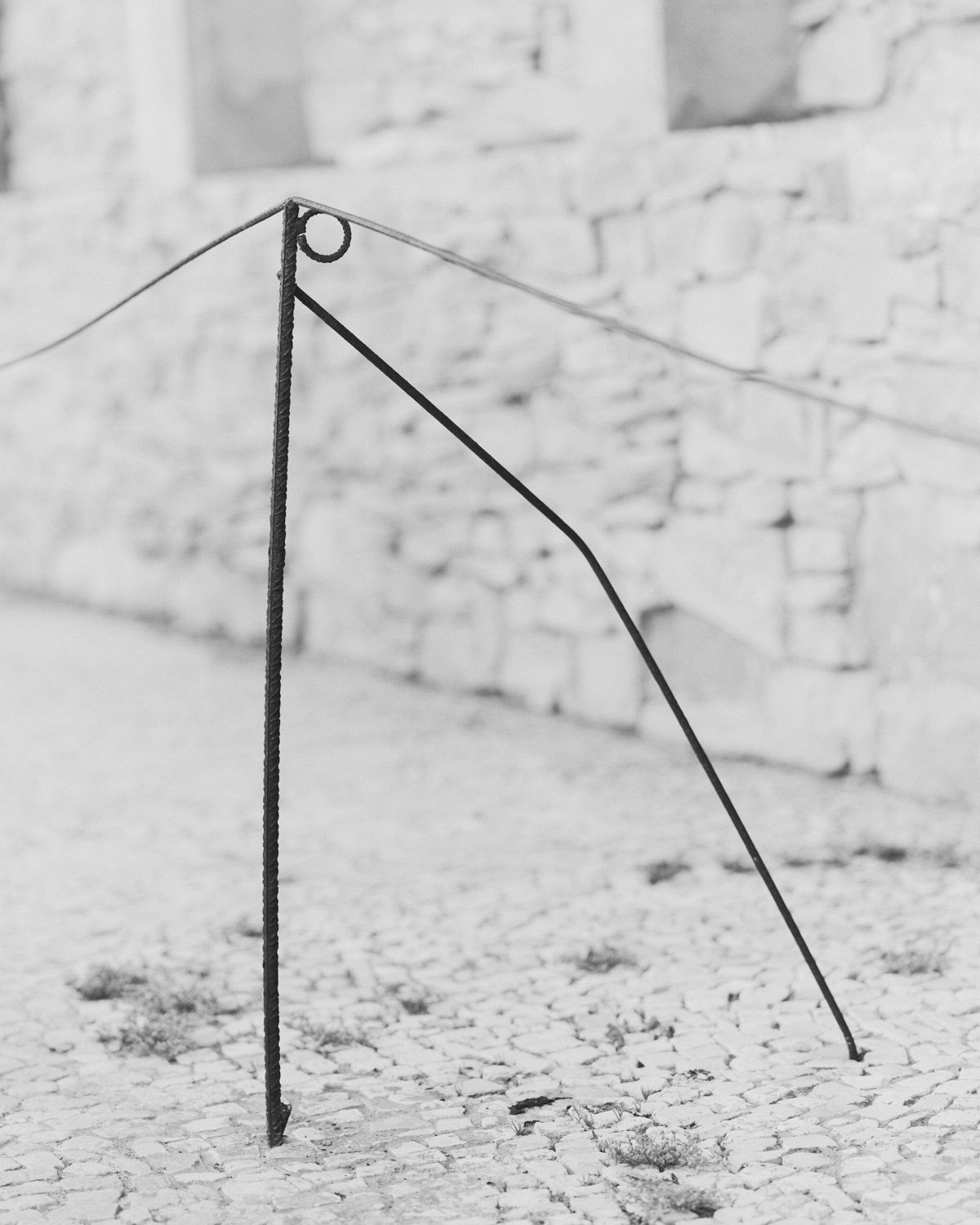 Struttura di metallo arrugginito su un terreno di pietre e un muro di pietra sullo sfondo.