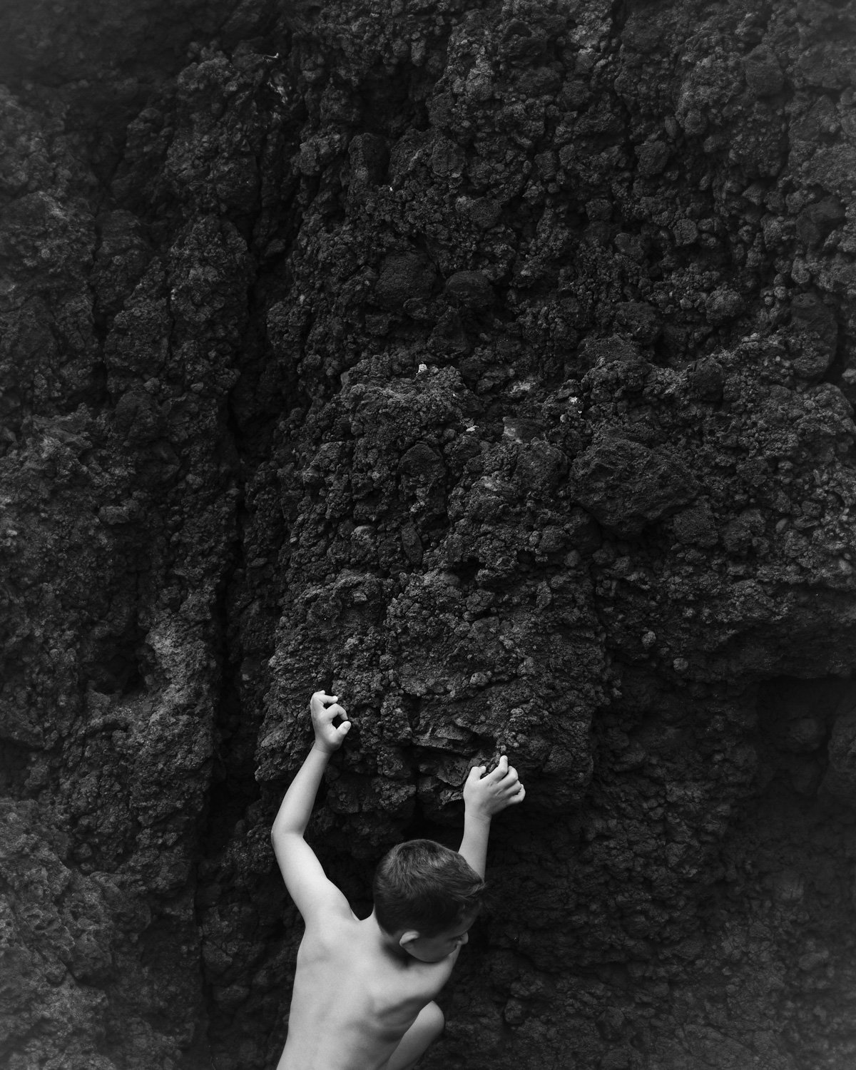 Un bambino nudo che si arrampica su una parete rocciosa nera.