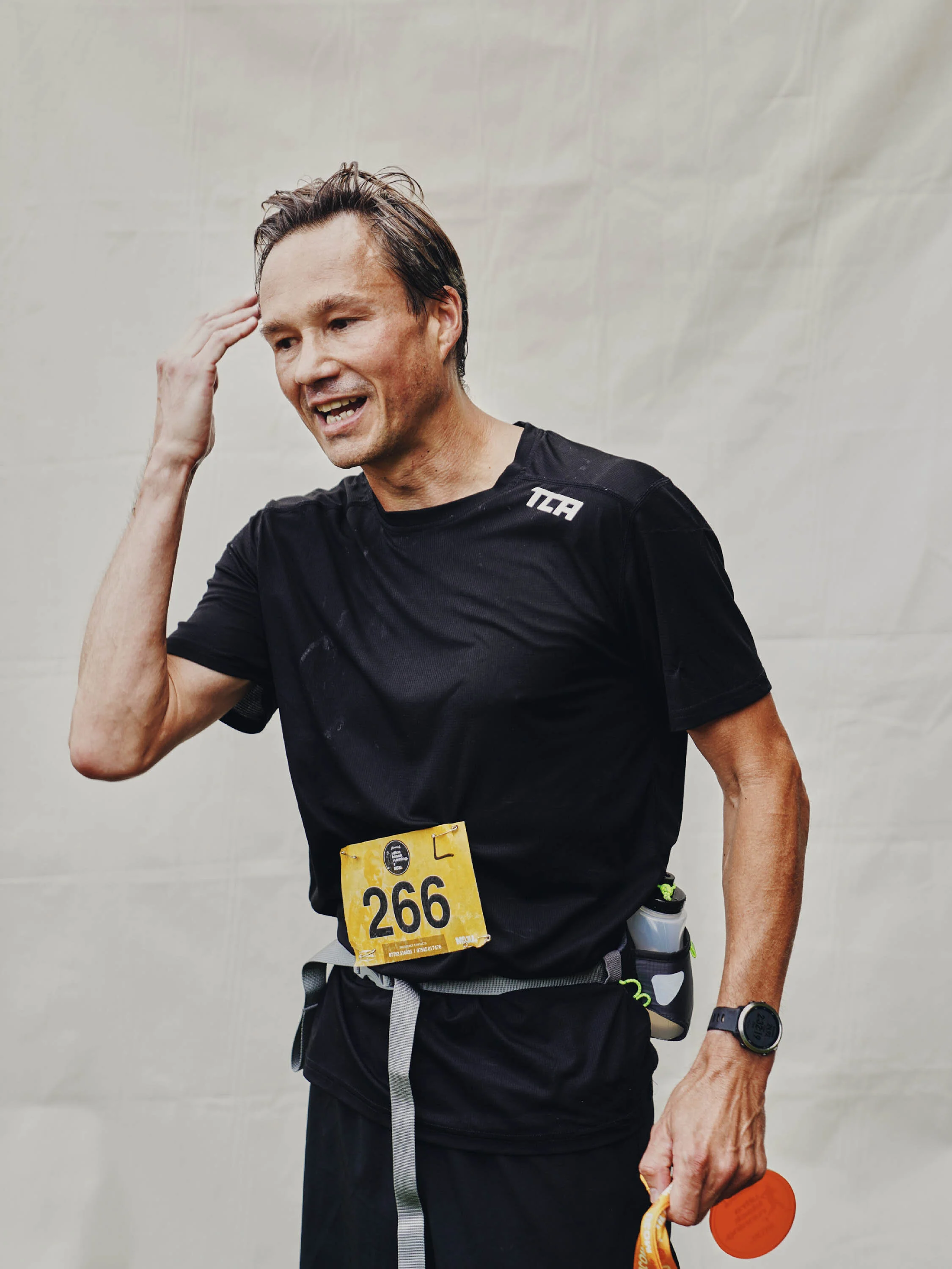 Male marathon runner with race bib number 266, wearing a black shirt and holding a medal, appears exhausted after finishing a race.