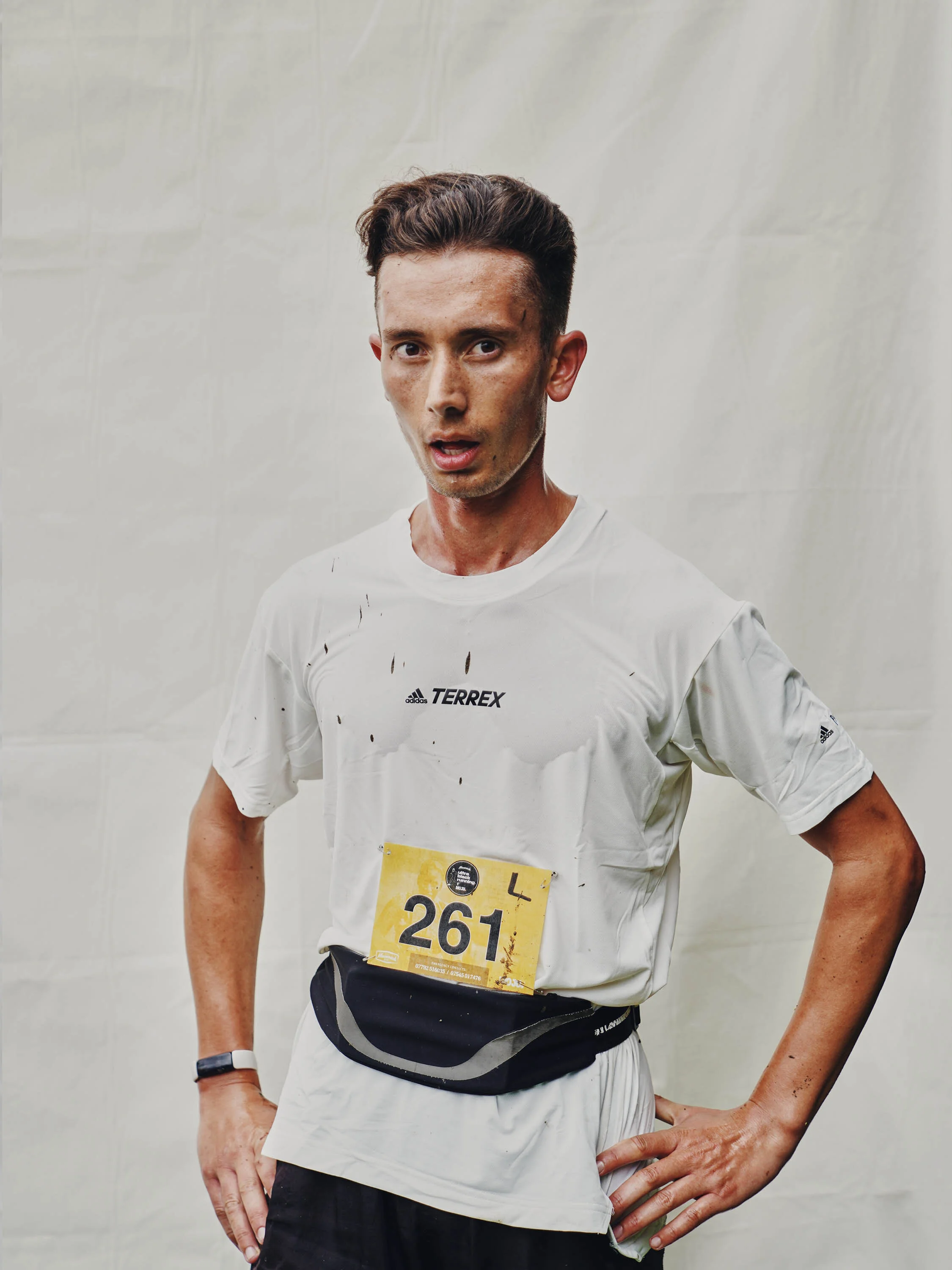 A male runner with a race bib number 261, wearing athletic gear, standing with hands on hips, looking tired after running.