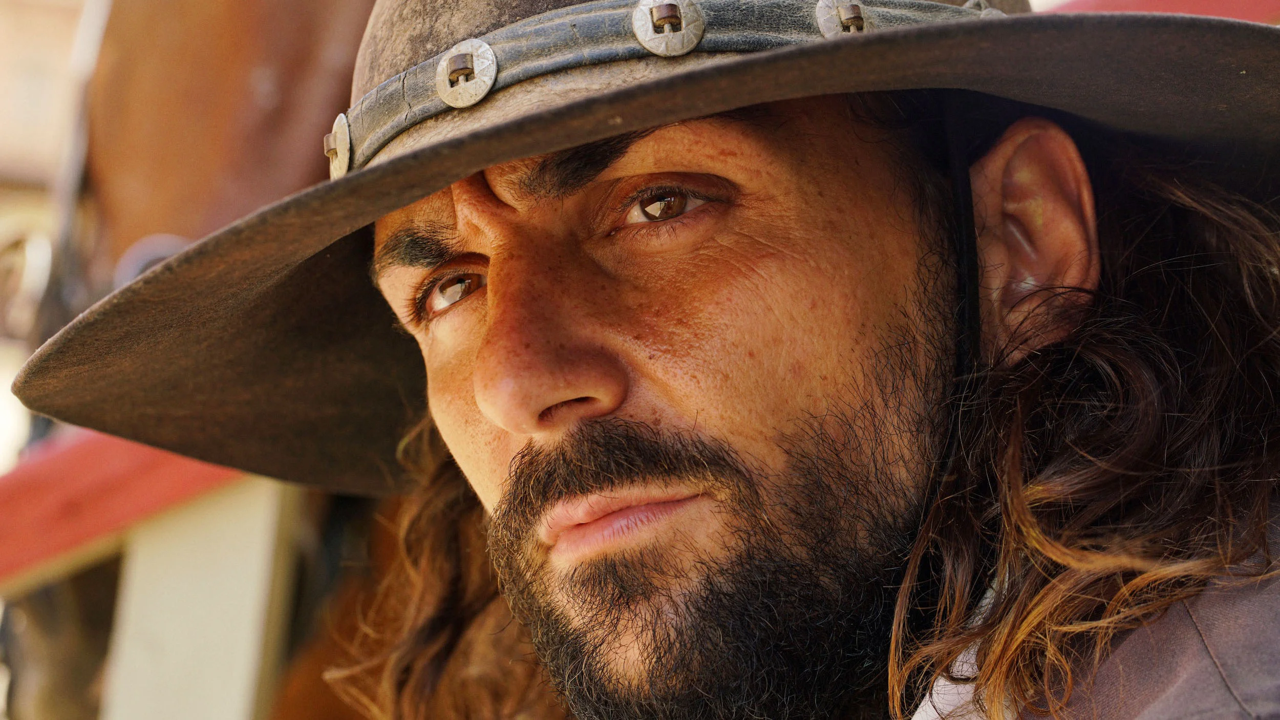 Close-up of a man with a beard and long hair wearing a cowboy hat, looking serious.