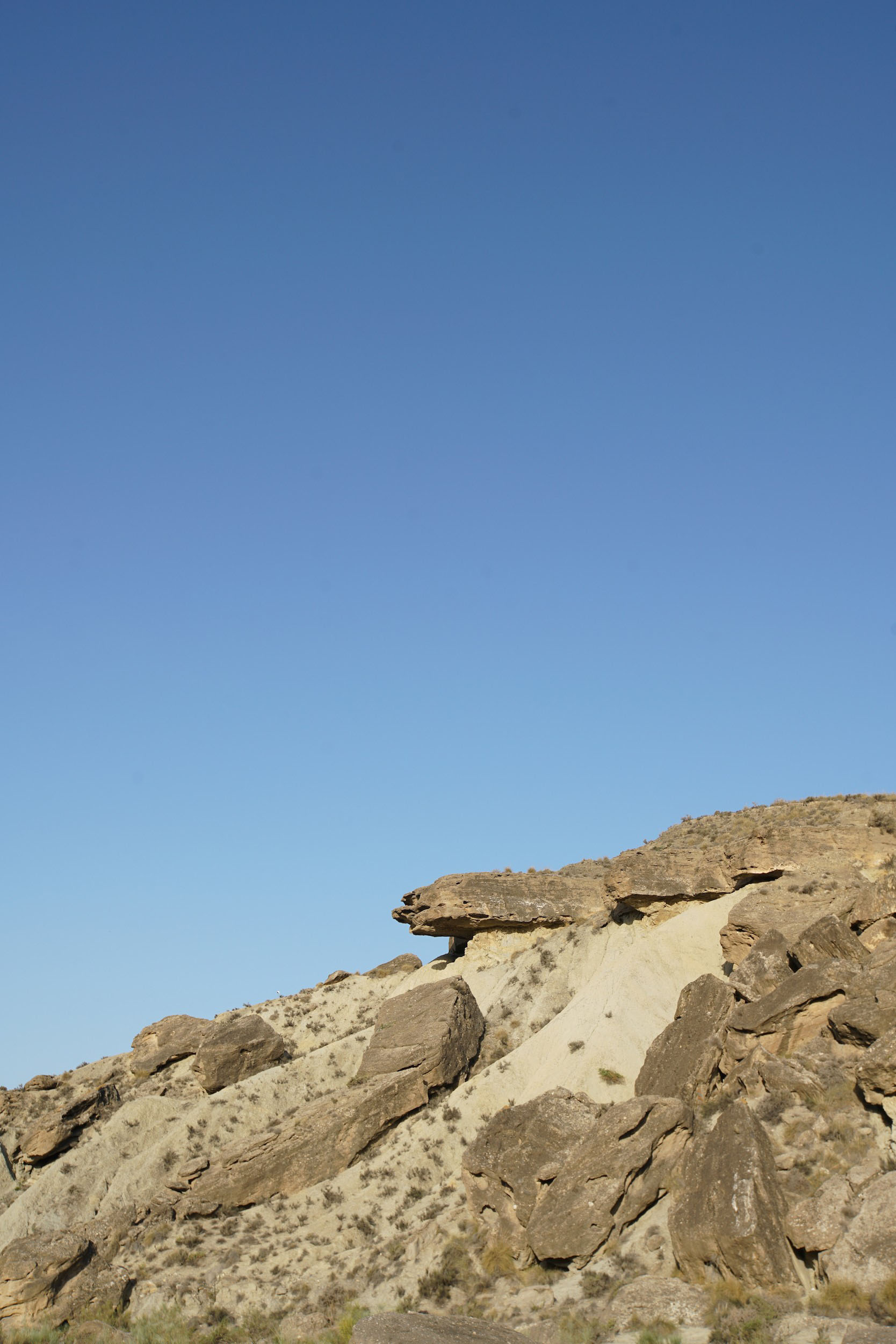 A desert landscape with large rocks and sandy hills under a clear blue sky.