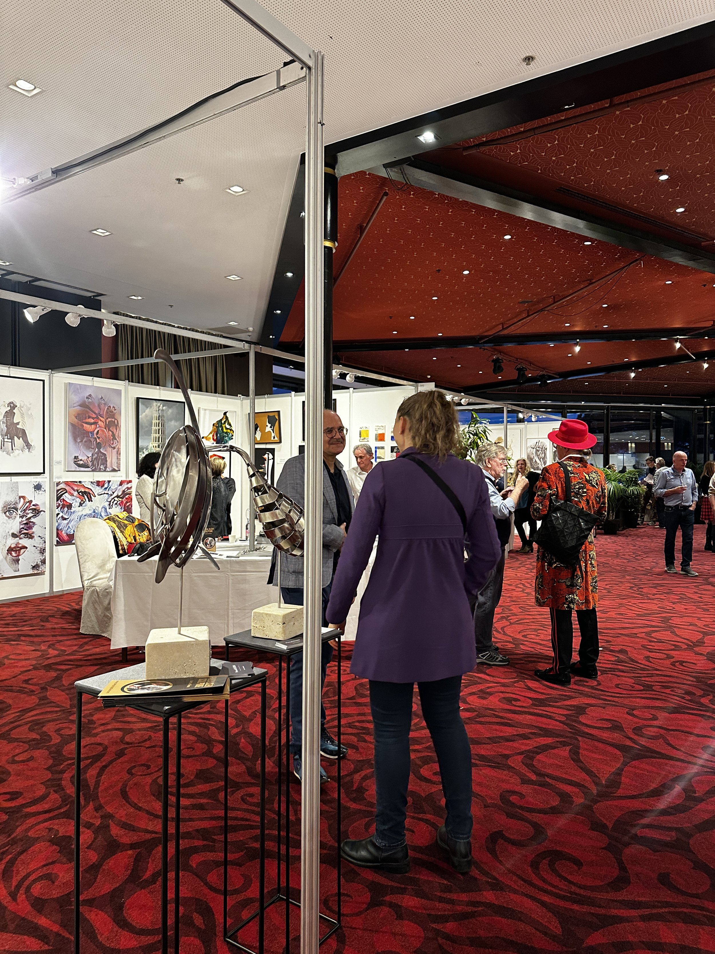 Vue d'un salon d'art avec plusieurs personnes qui regardent des œuvres d'art et des sculptures exposées.