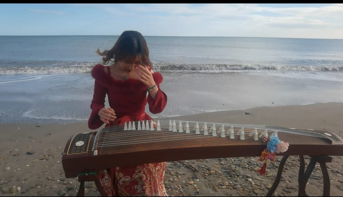 Une femme jouant du guzheng sur la plage avec la mer en arrière-plan.