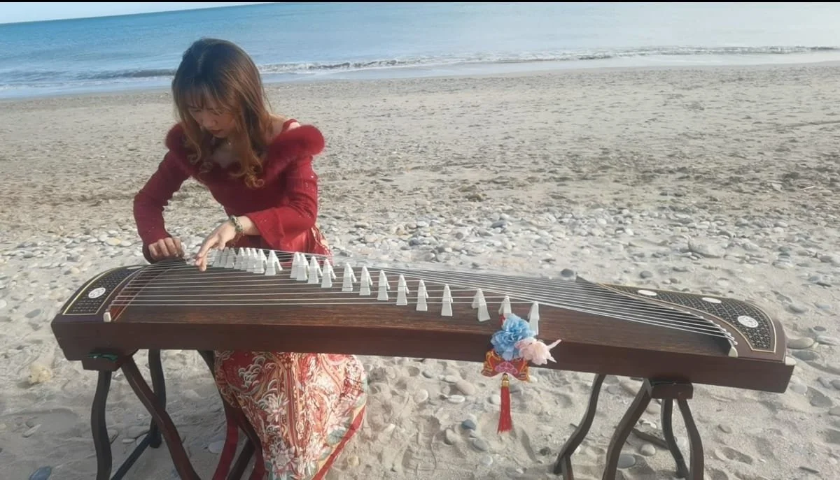 Une femme joue d'une guzheng sur la plage.