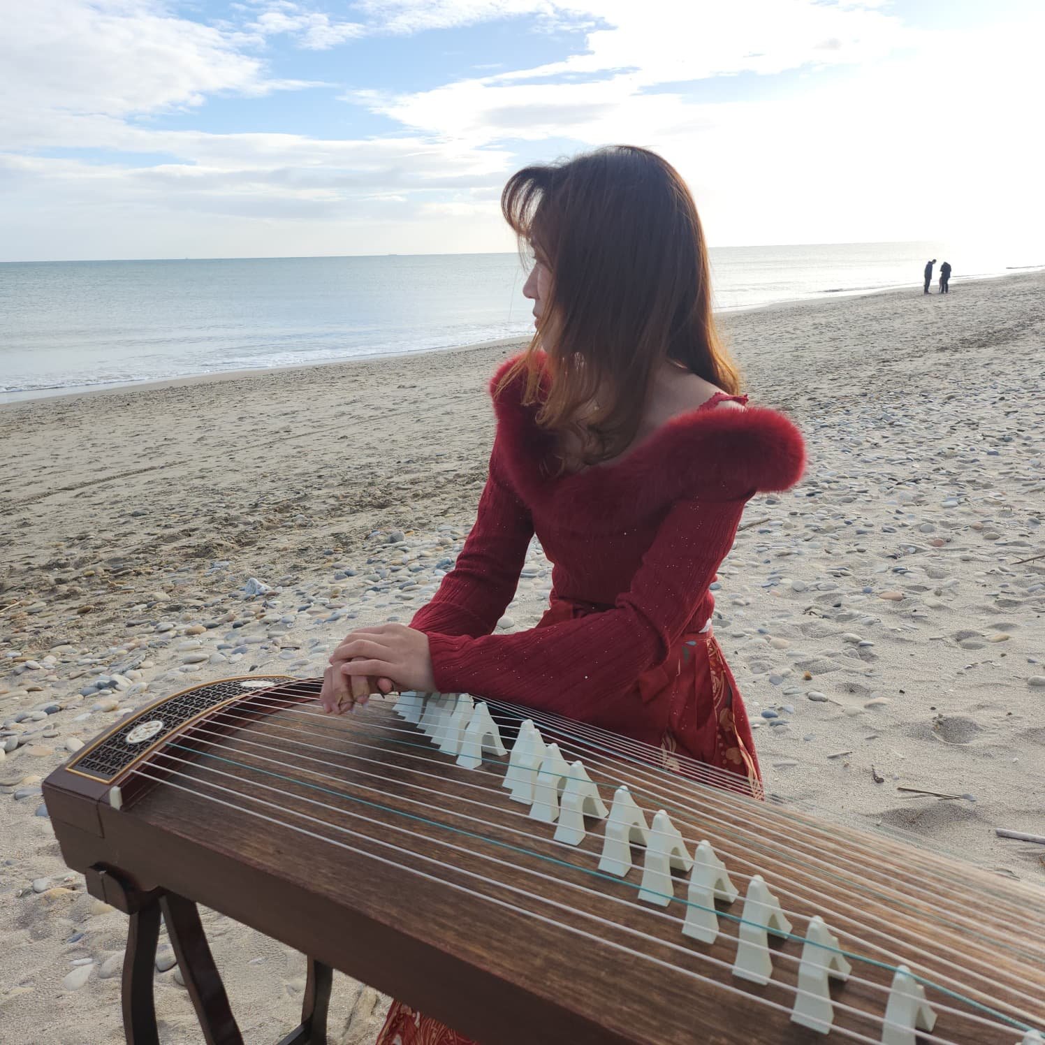 Une femme joue du guzheng sur la plage, avec la mer et le ciel en arrière-plan.