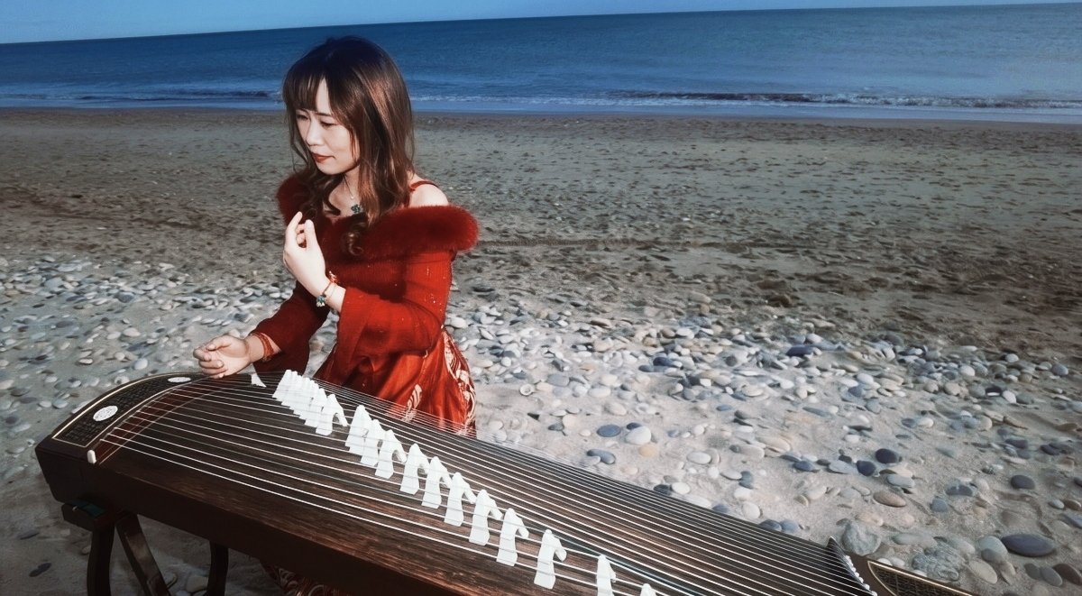 Femme jouant du guzheng sur la plage au coucher du soleil.