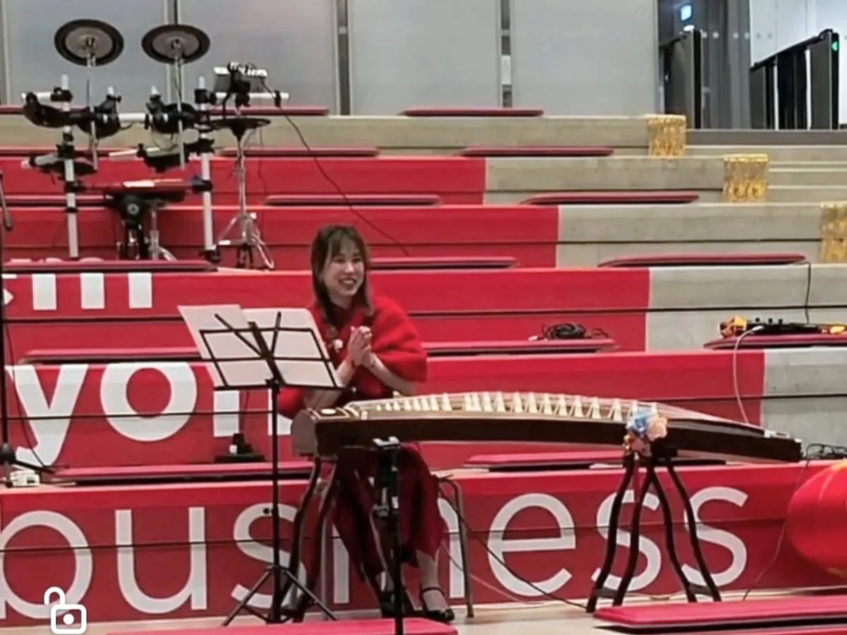 Une femme jouant d'un instrument traditionnel dans une salle avec des escaliers rouges, entourée de matériel de musique et de câbles.