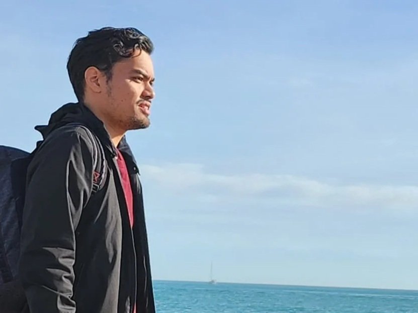 Un homme avec un sac à dos regarde l'océan par temps clair.