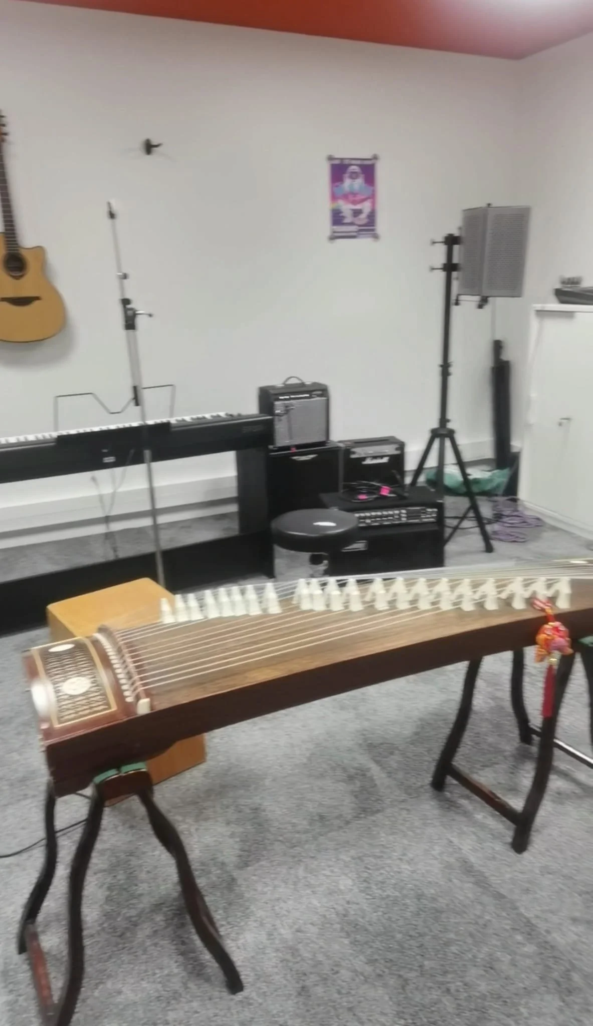 Salle de musique avec guitare accrochée au mur, clavier, microphones, amplificateurs, instrument occitan, et équipement de sonorisation.