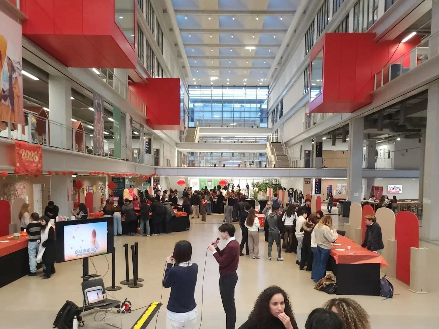 Une grande halle d'aéroport ou centre commercial avec plusieurs personnes, des tables, et des décorations rouges et or pour célébrer le Nouvel An chinois.
