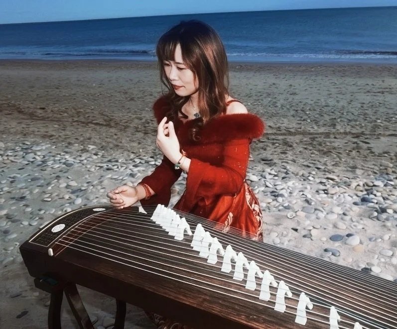 Une femme joue du guqin sur la plage au coucher du soleil.