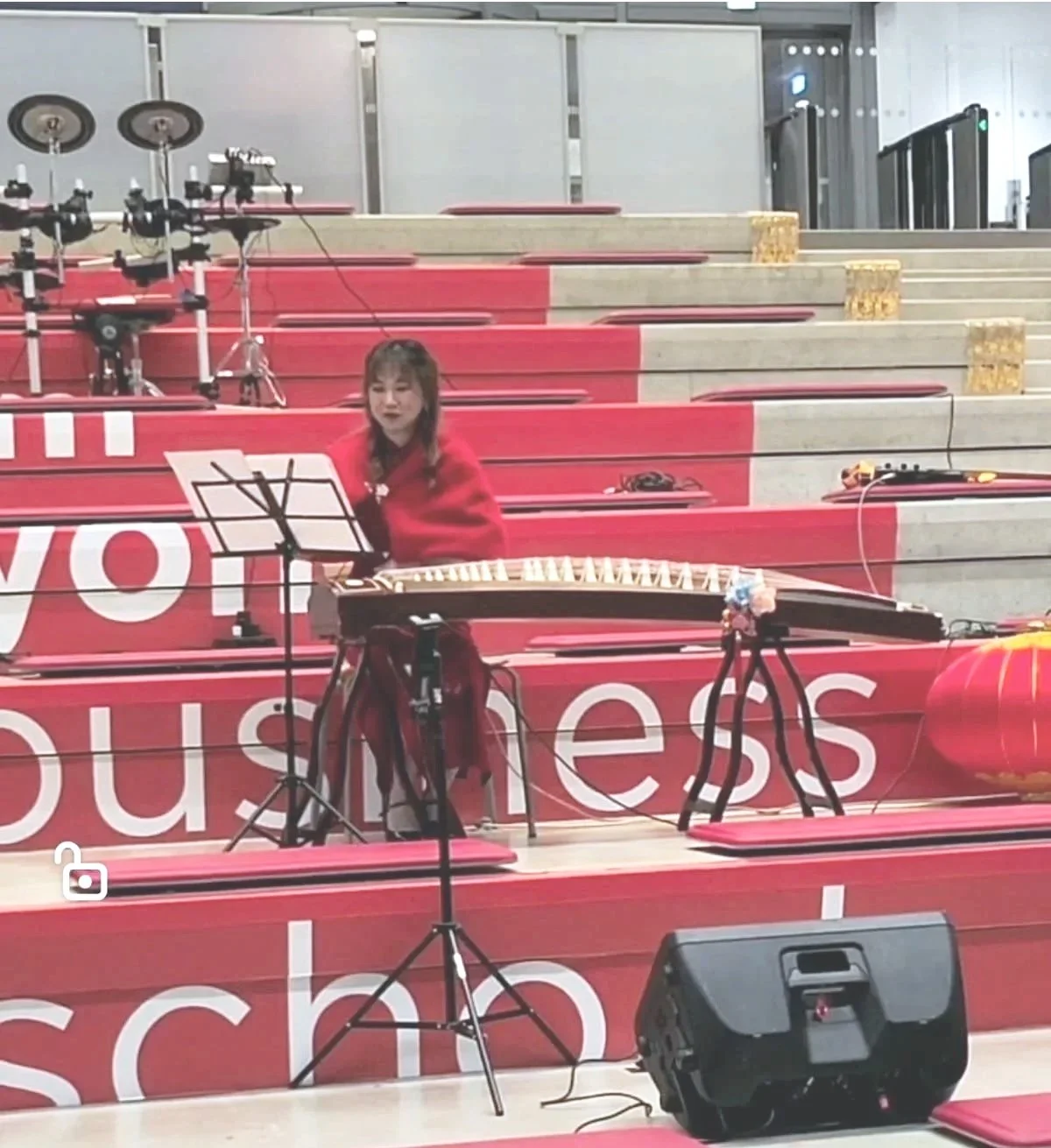une femme joue du guzheng dans un espace sans public, avec des chaises rouges et un sonorisateur