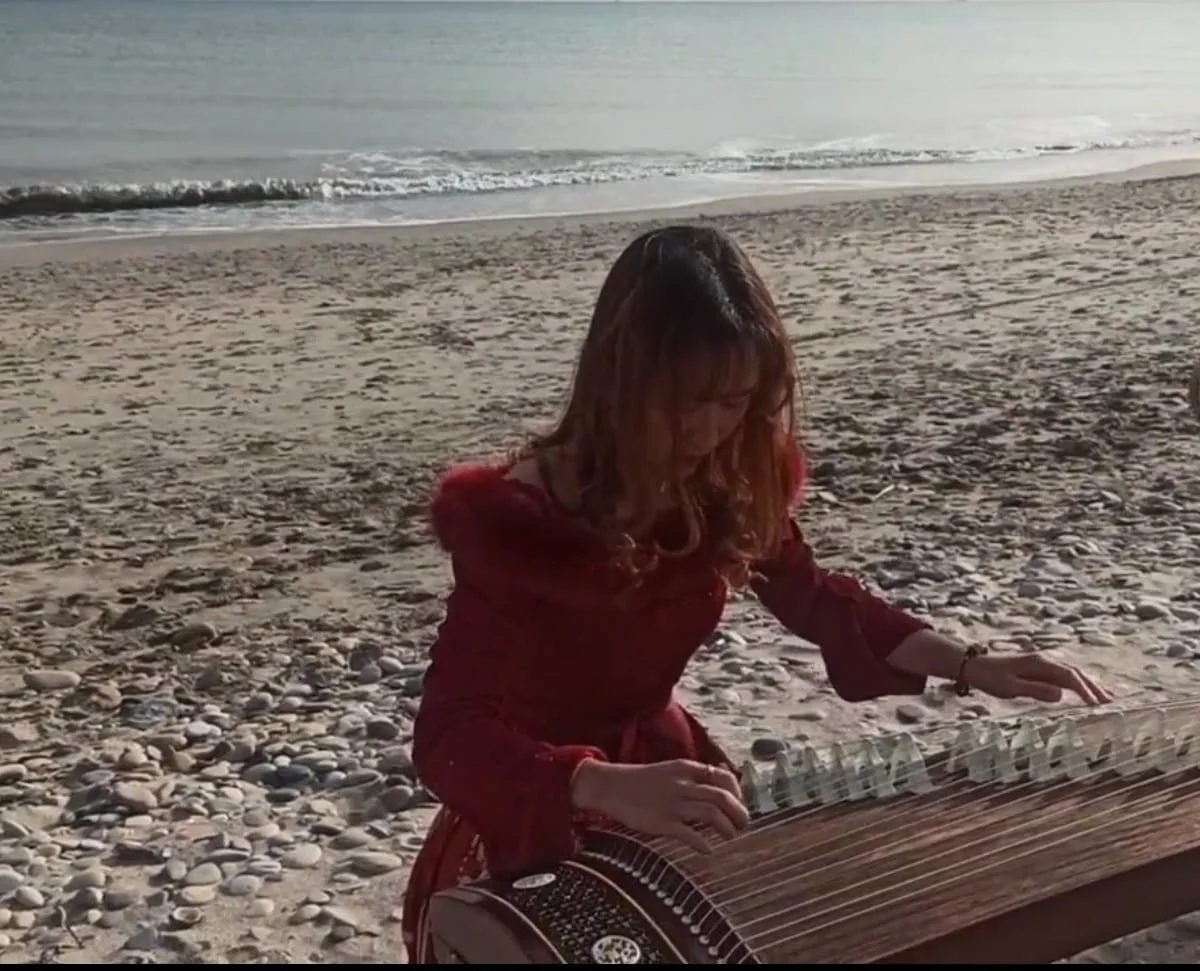 Une femme jouant du qanun sur la plage au coucher du soleil.