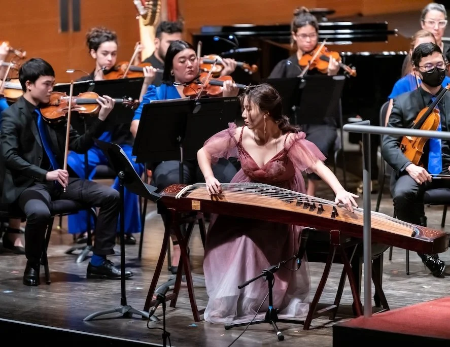 Une femme joue du konghou lors d'un concert avec un orchestre symphonique.