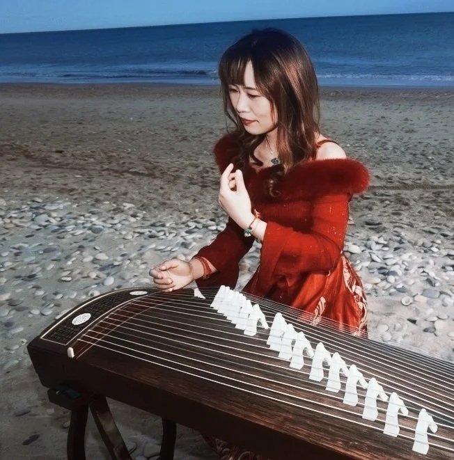 Une femme jouant du guzheng sur la plage au coucher du soleil.