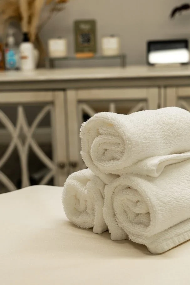 Four neatly rolled white towels on a table in a room with a gray cabinet in the background.